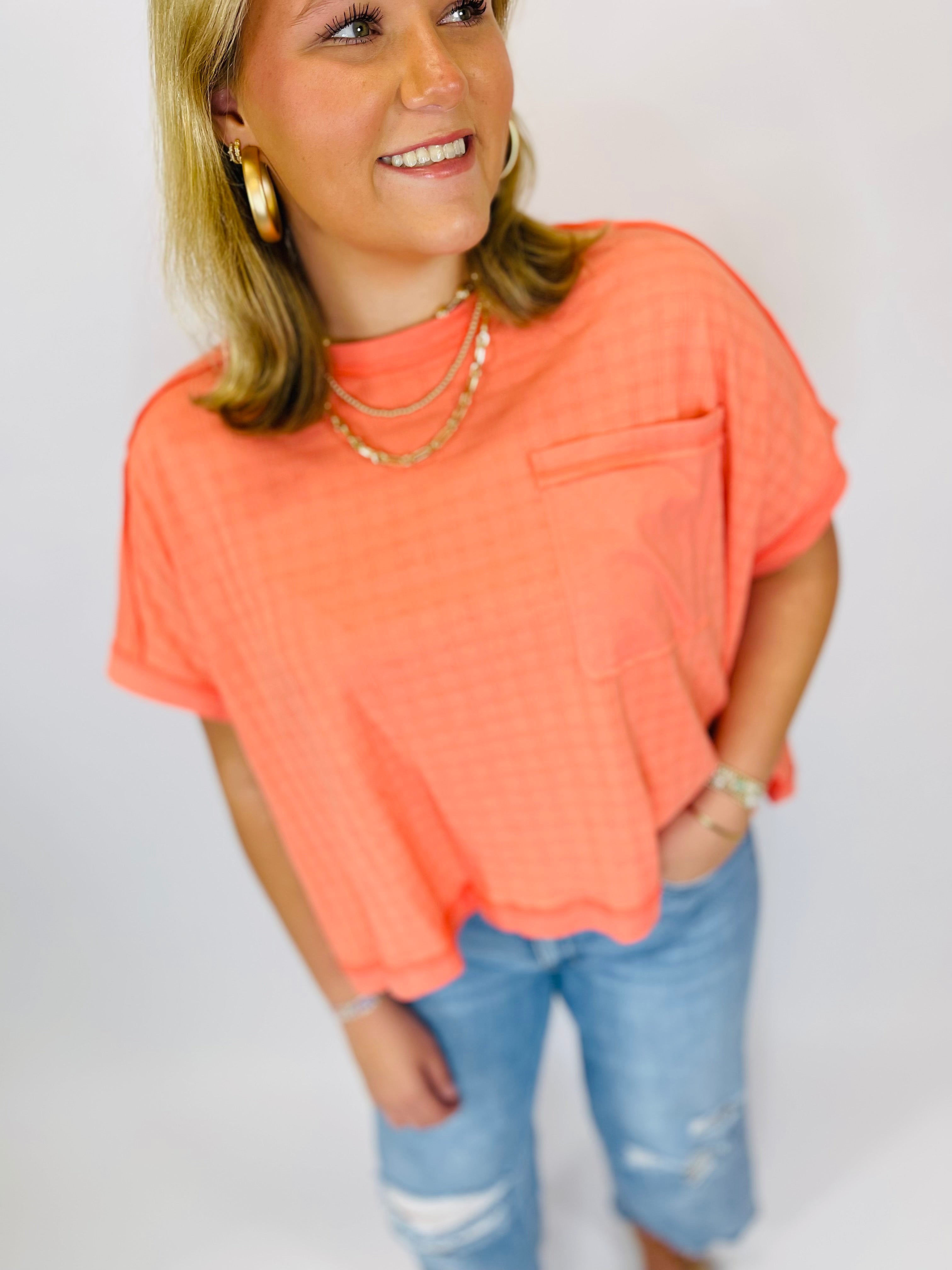 Woman wearing coral oversized short-sleeve top with layered gold necklaces and distressed blue jeans
