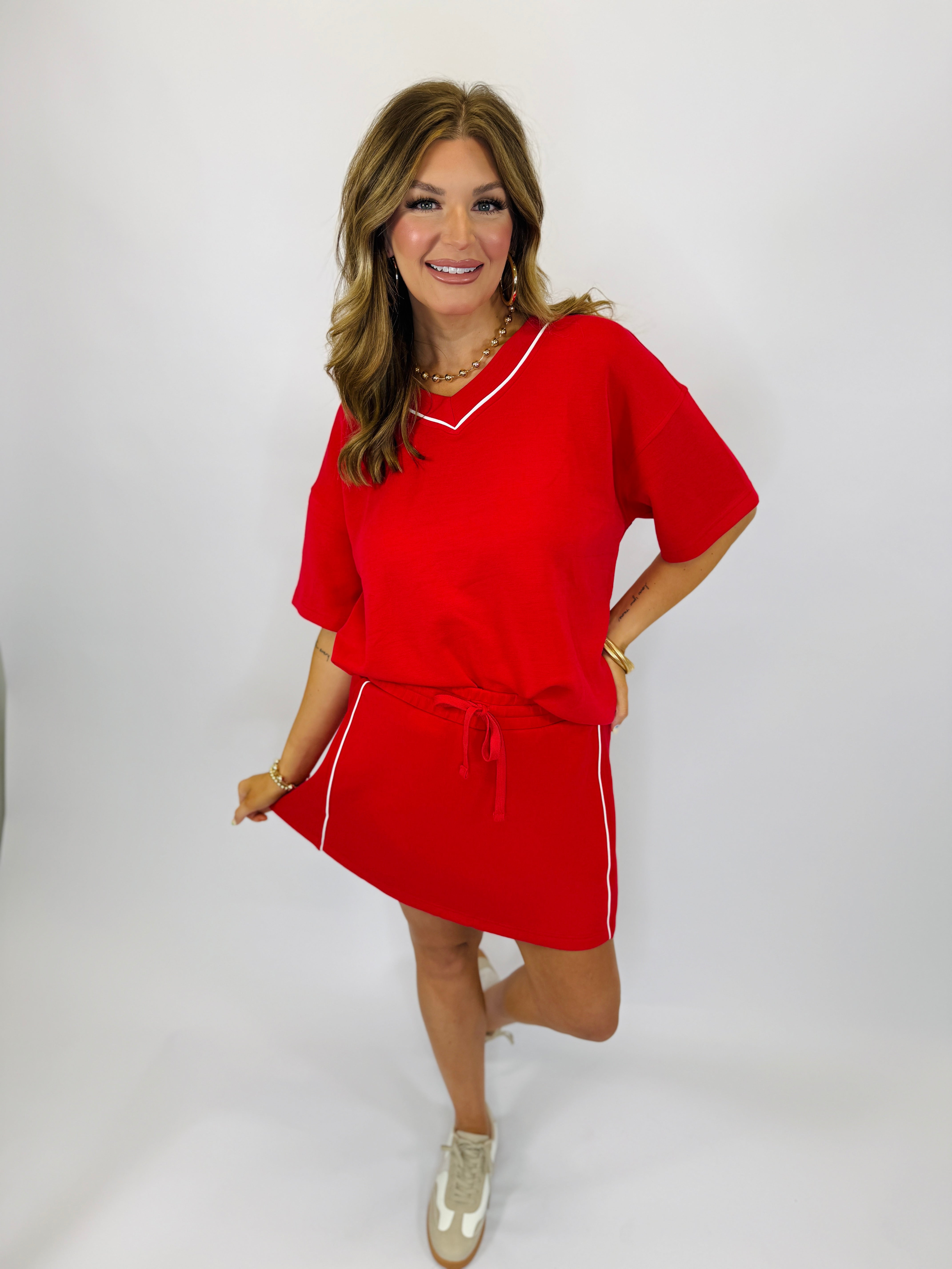 Woman wearing red athletic dress with white trim and drawstring waist, styled with gold sneakers and jewelry.
