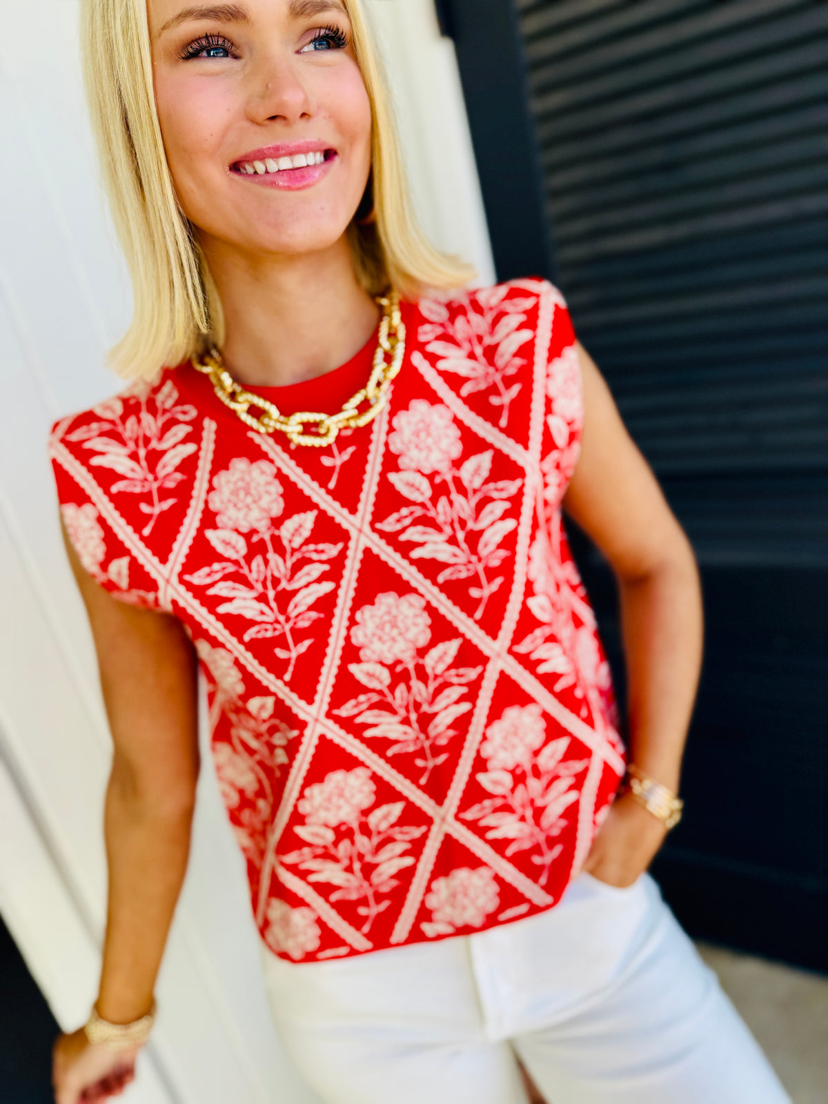 Woman wearing red floral patterned Lola Meadow soft top with white geometric lines and gold chain necklace