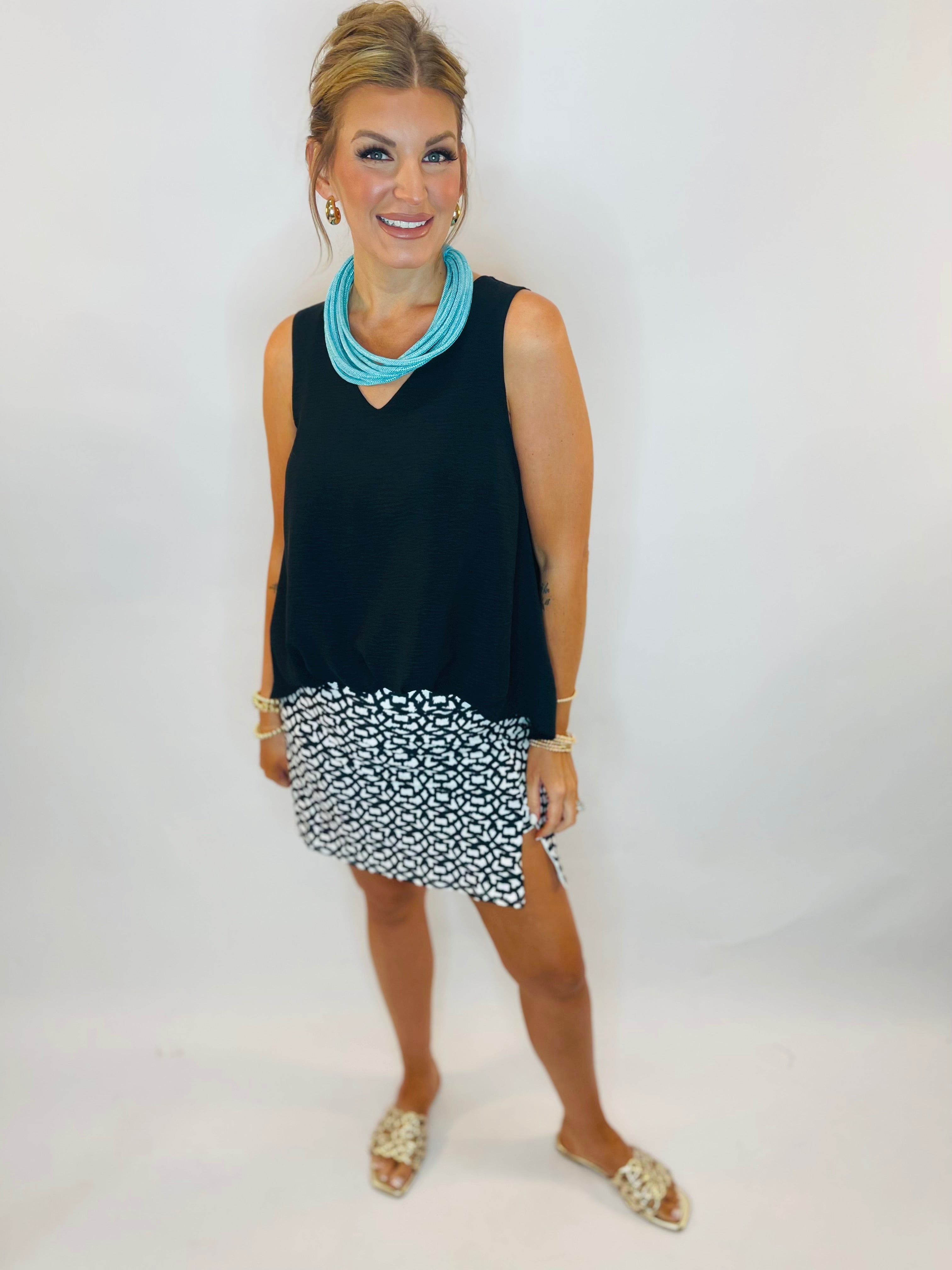 Black sleeveless V-neck tank top styled with black and white patterned mini skirt and turquoise necklace.