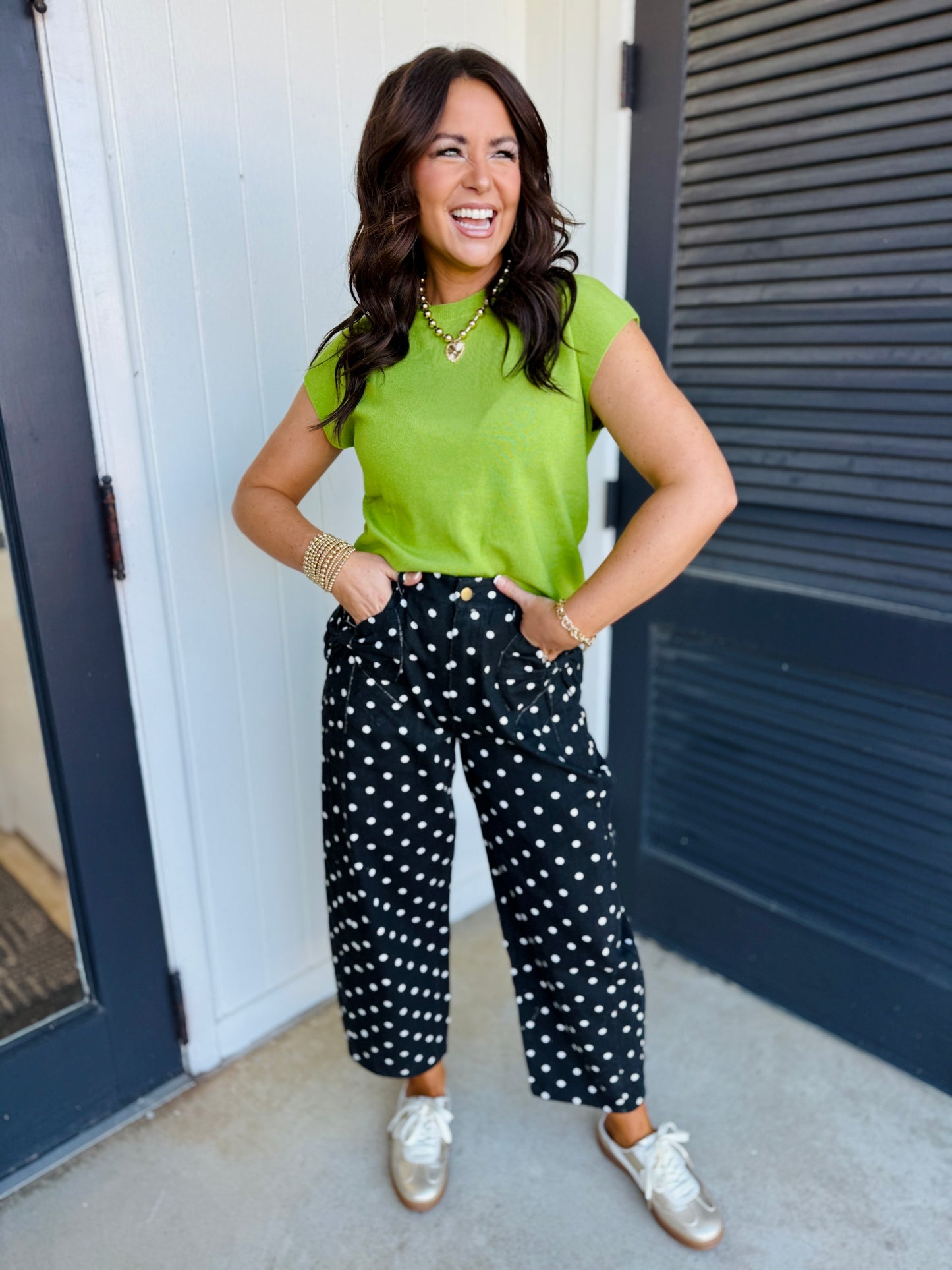 Woman wearing black polka dot wide-leg pants with green top and white sneakers, smiling outdoors