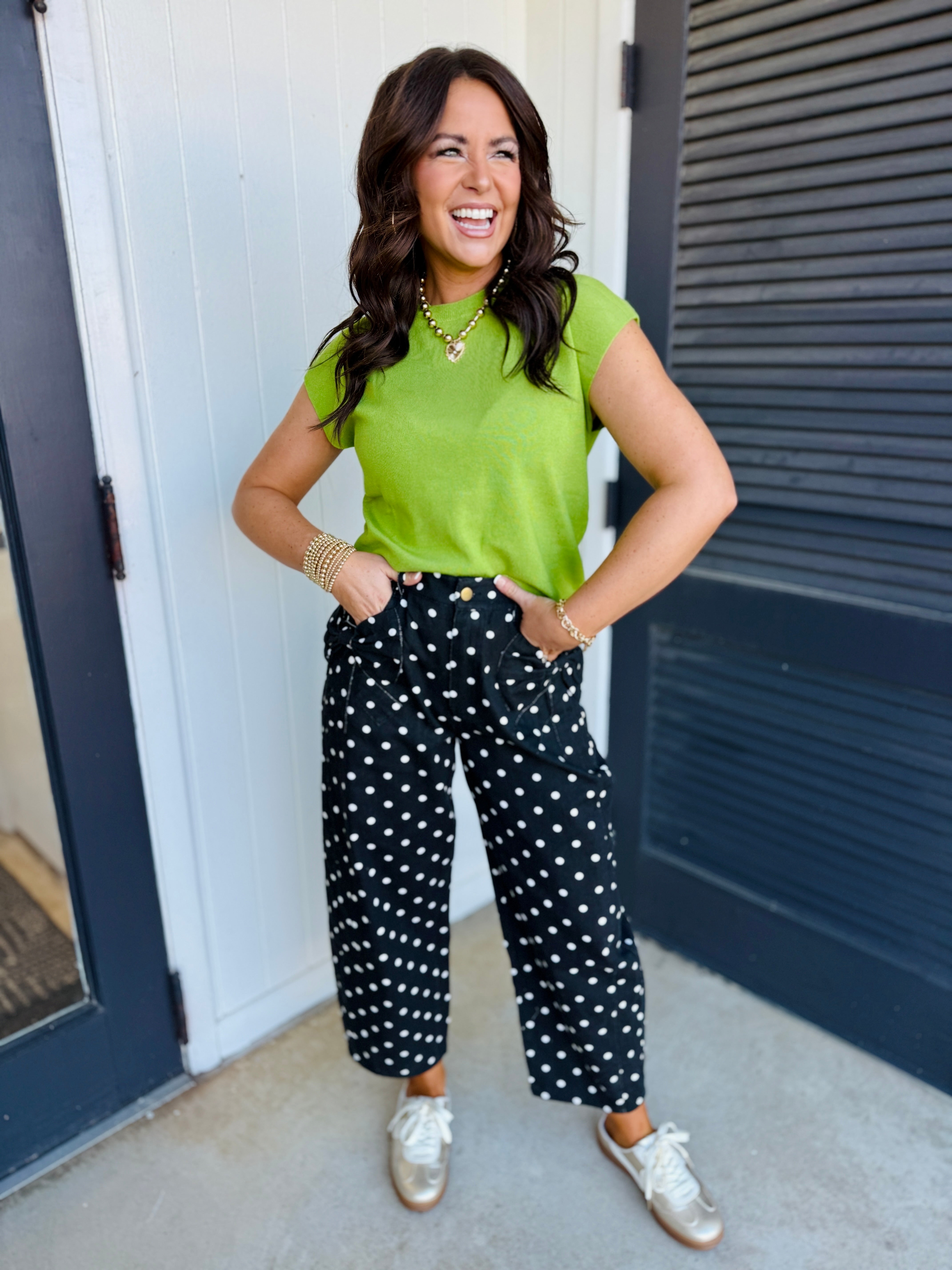 Woman wearing black polka dot wide-leg pants with green top and white sneakers, smiling outdoors