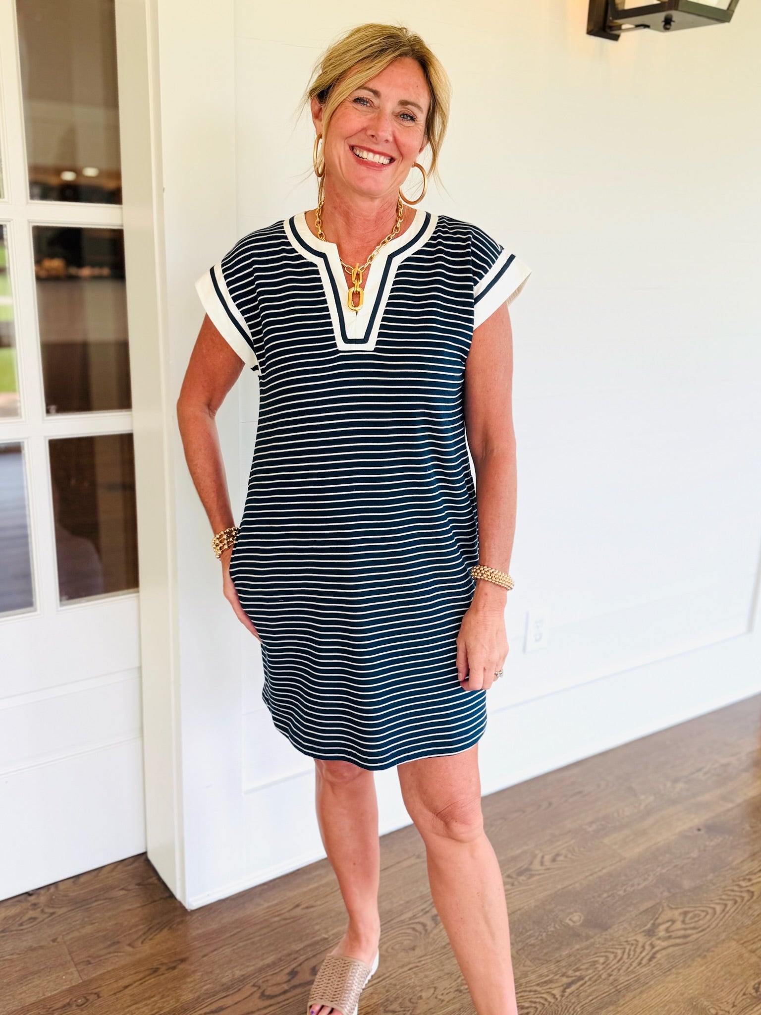 Navy and white striped short-sleeve shift dress with white V-neckline trim, worn by smiling woman.
