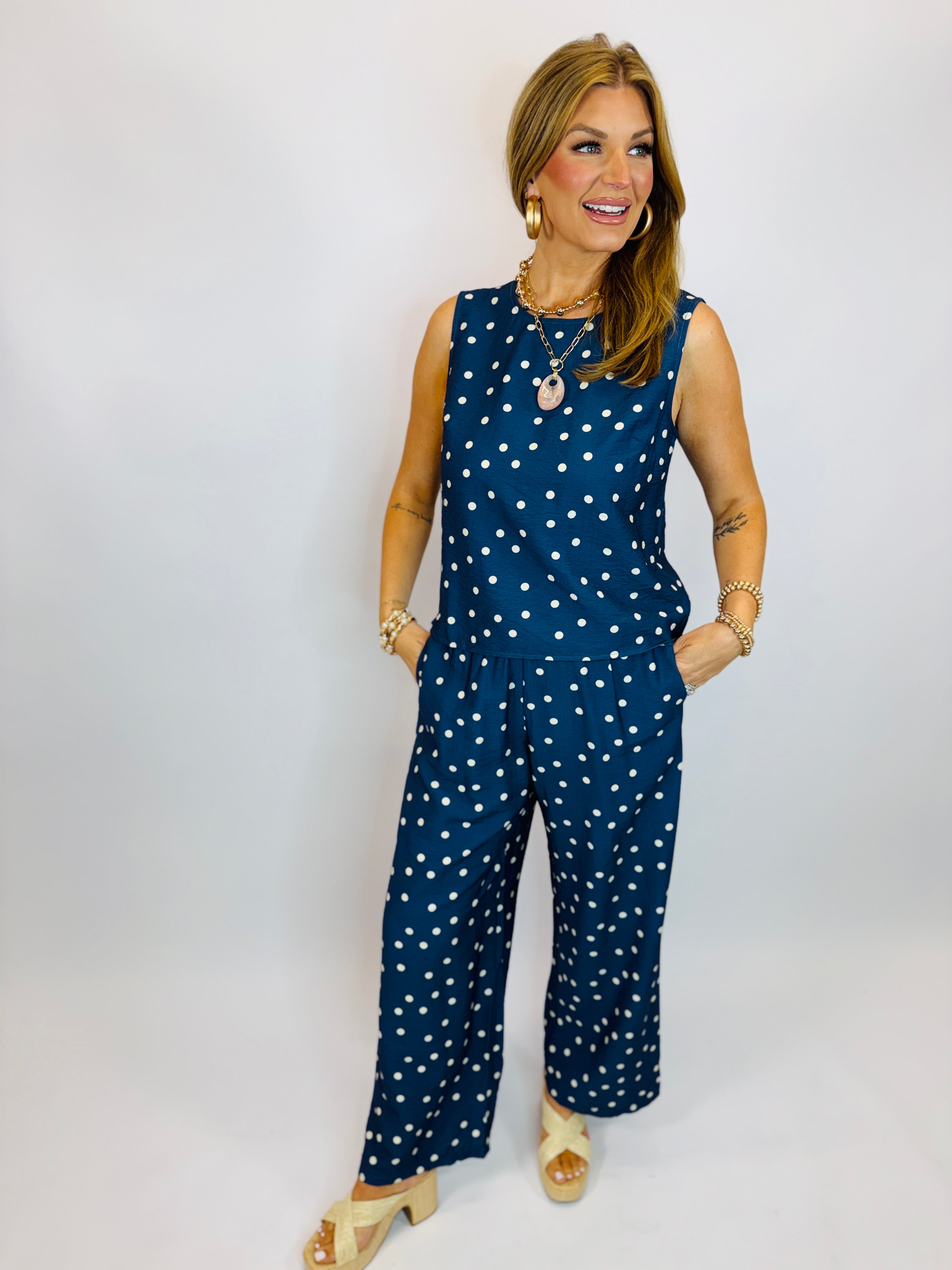 Navy blue polka dot sleeveless top and matching wide-leg pants set worn by smiling woman with gold jewelry.