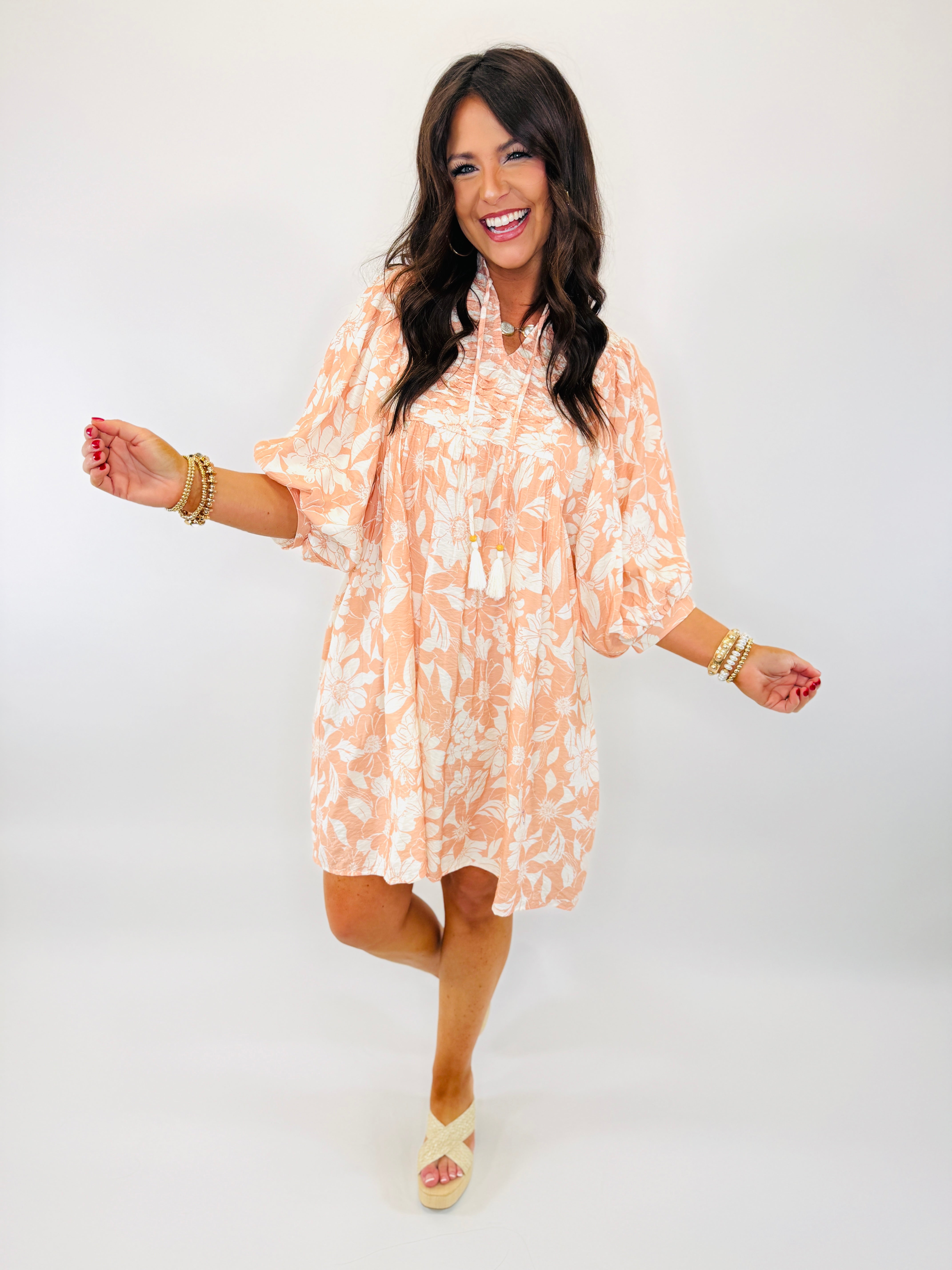 Woman wearing orange and white floral Rebecca dress with three-quarter sleeves, posing with arms outstretched and smiling.