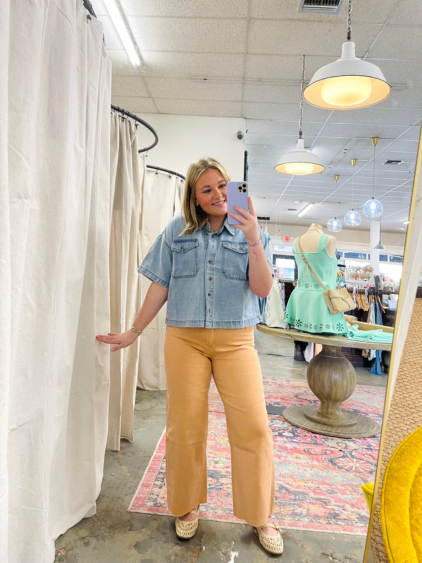 Woman wearing light blue short-sleeve denim shirt and mustard wide-leg pants in clothing store fitting area