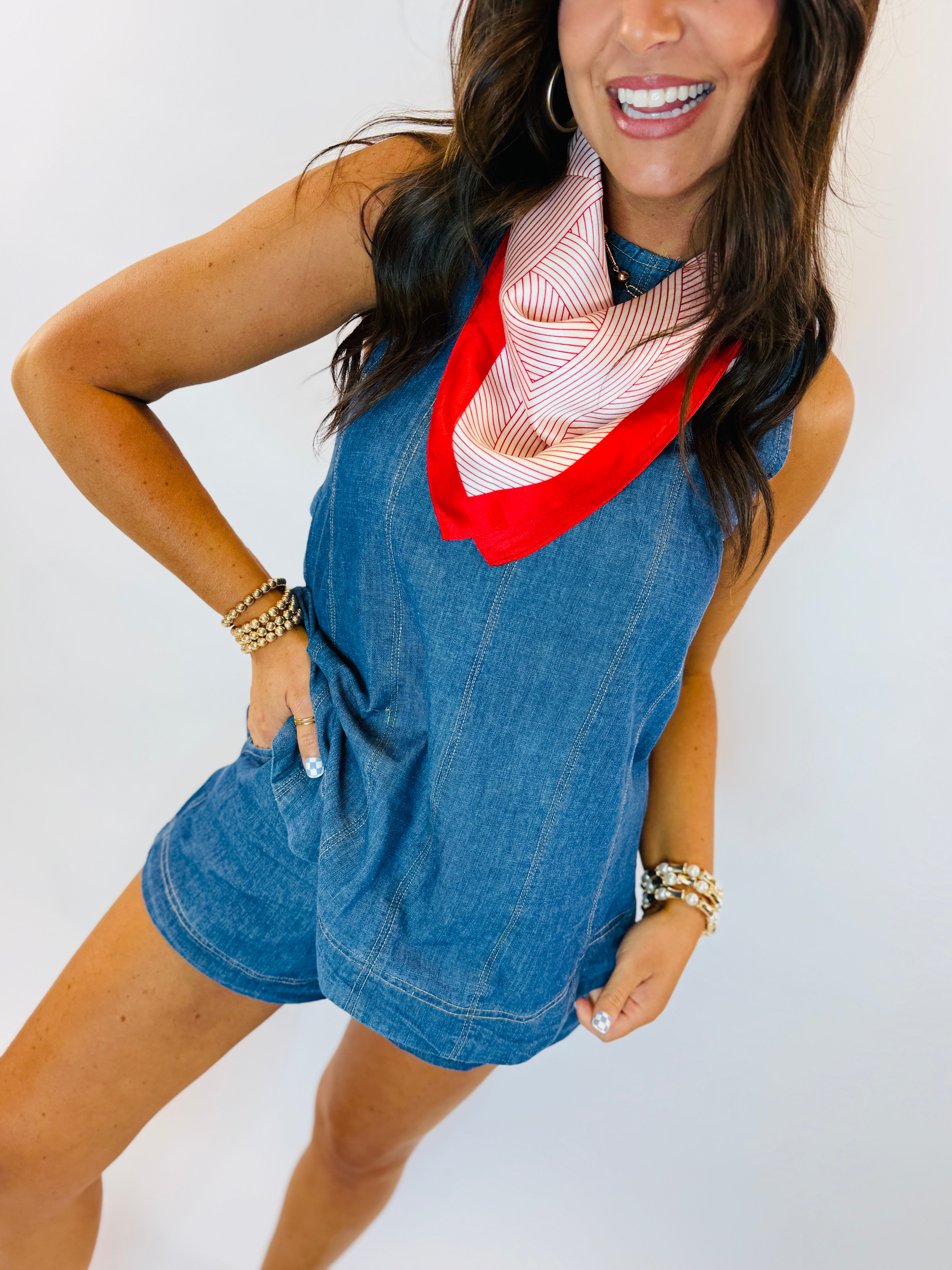 Woman wearing blue denim sleeveless top and shorts set with red and white striped scarf accessory.
