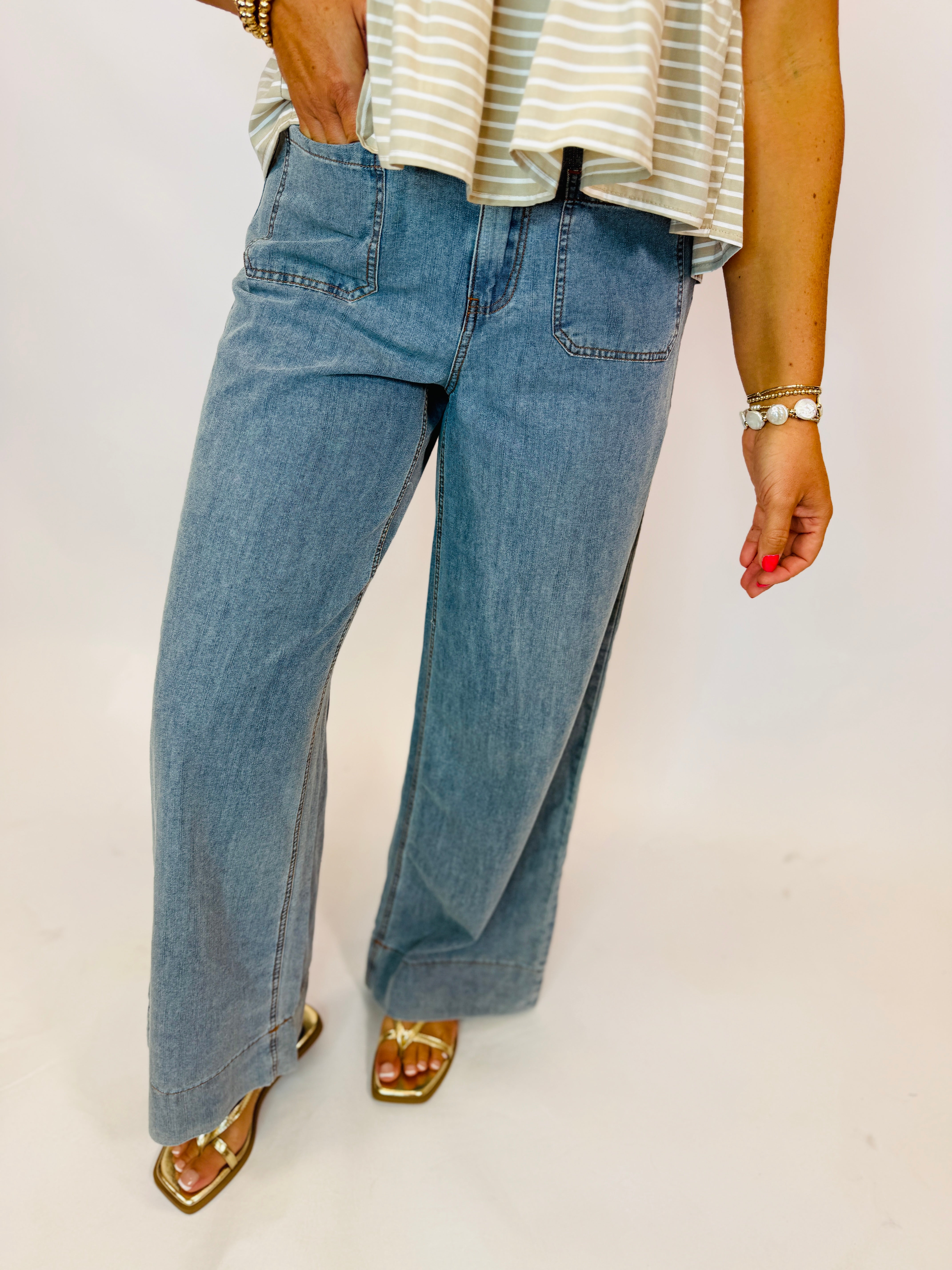 Light wash wide-leg denim jeans with front patch pockets, paired with gold sandals and striped top.
