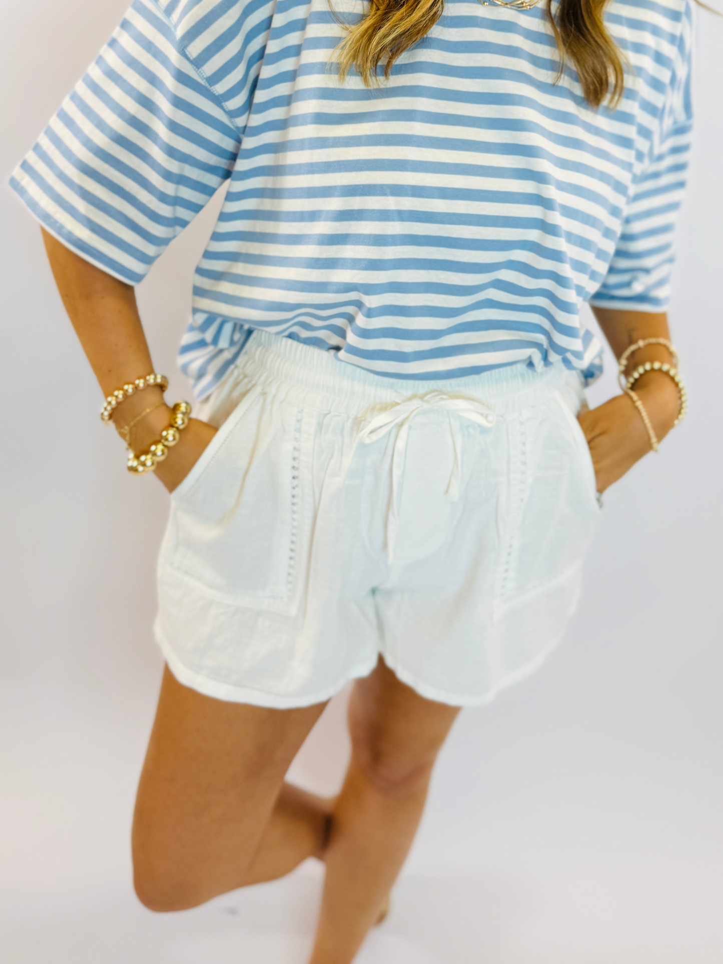 Woman wearing white drawstring shorts with blue and white striped top, styled with pearl bracelets.