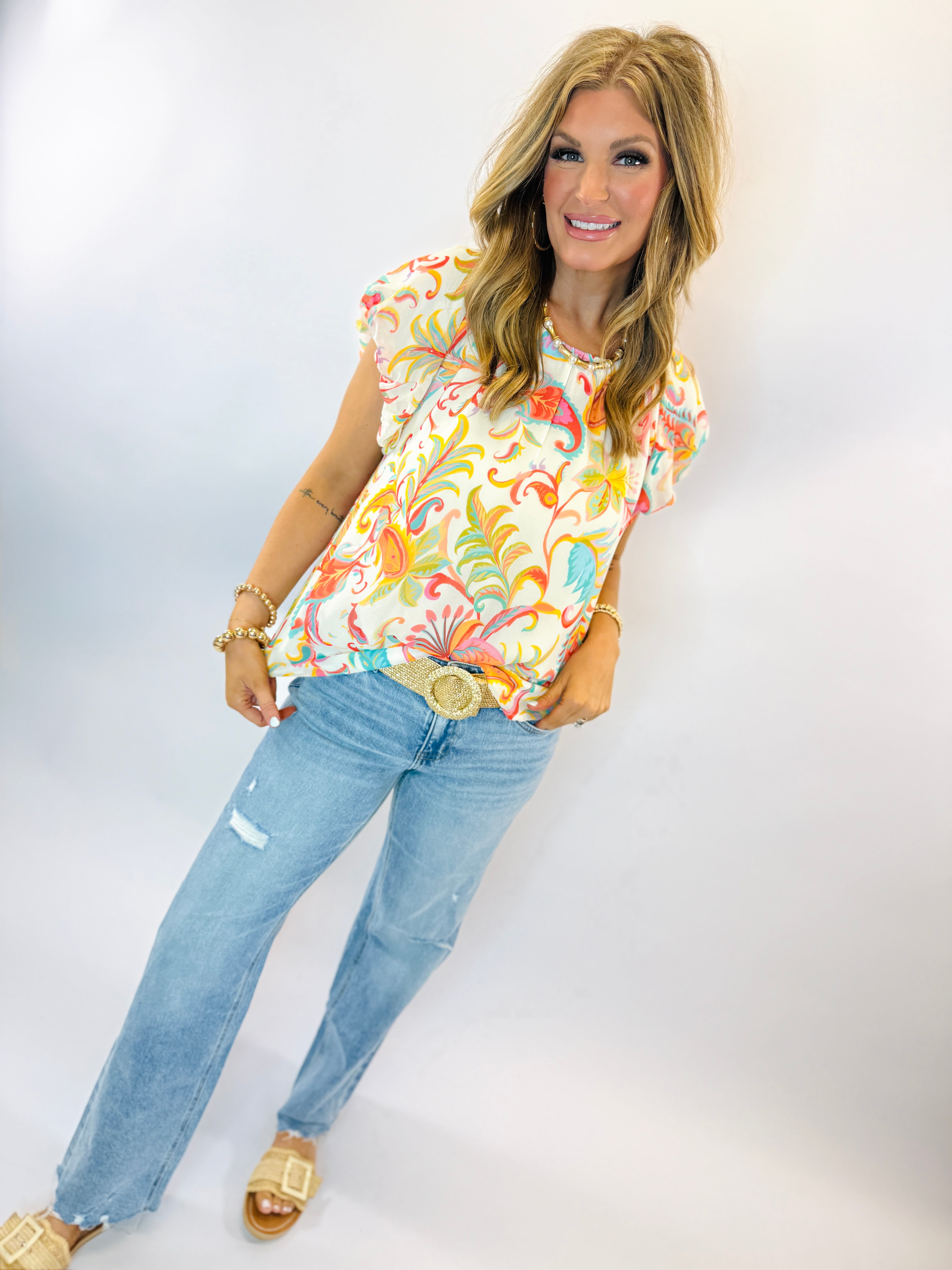 Woman wearing colorful floral print Mila top with short sleeves, paired with distressed jeans and gold accessories.