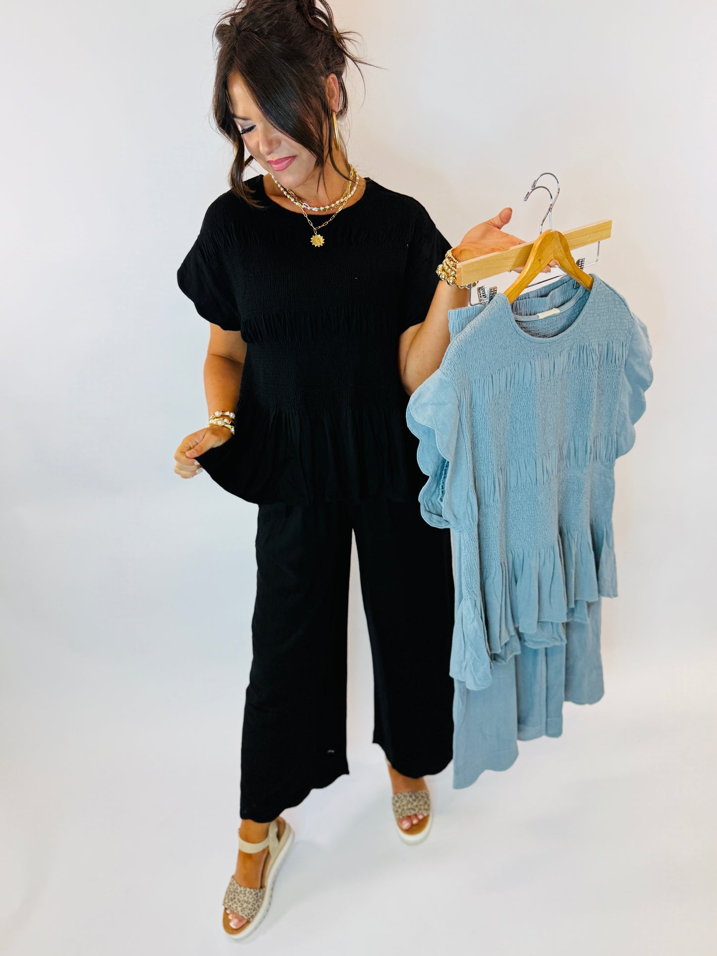 Woman in black outfit holding blue textured top and matching pieces on wooden hangers