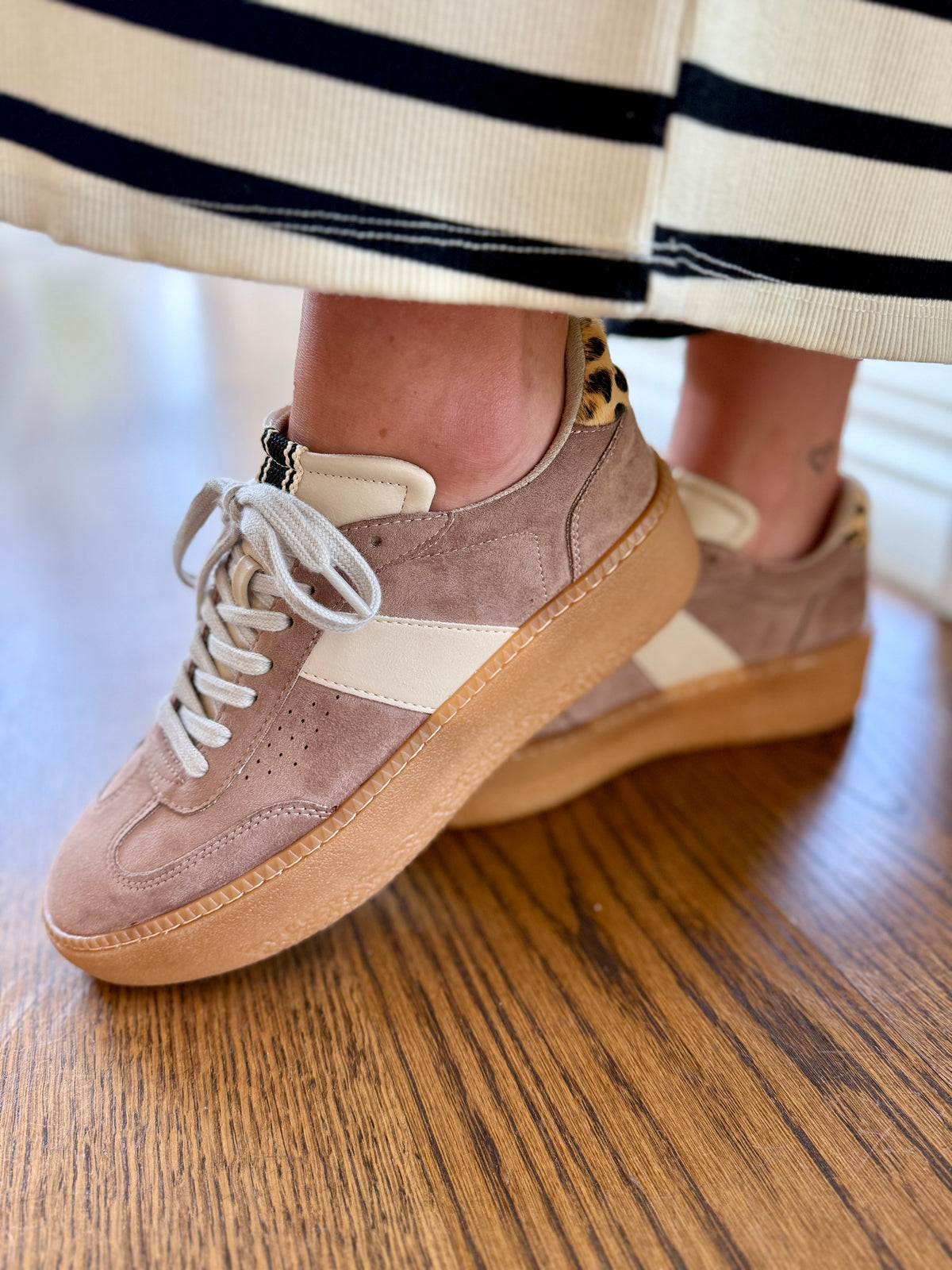 Tan suede Stacey sneakers with white laces and leopard print heel detail on wooden floor