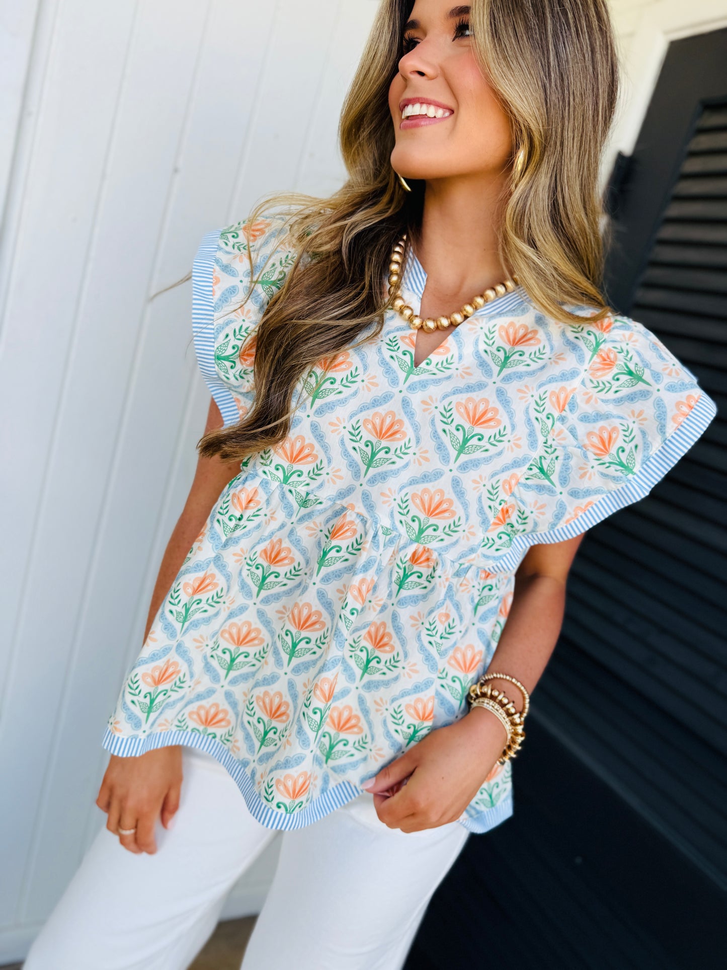 Woman wearing floral patterned Ella Everyday Turner Top with blue striped trim and white pants