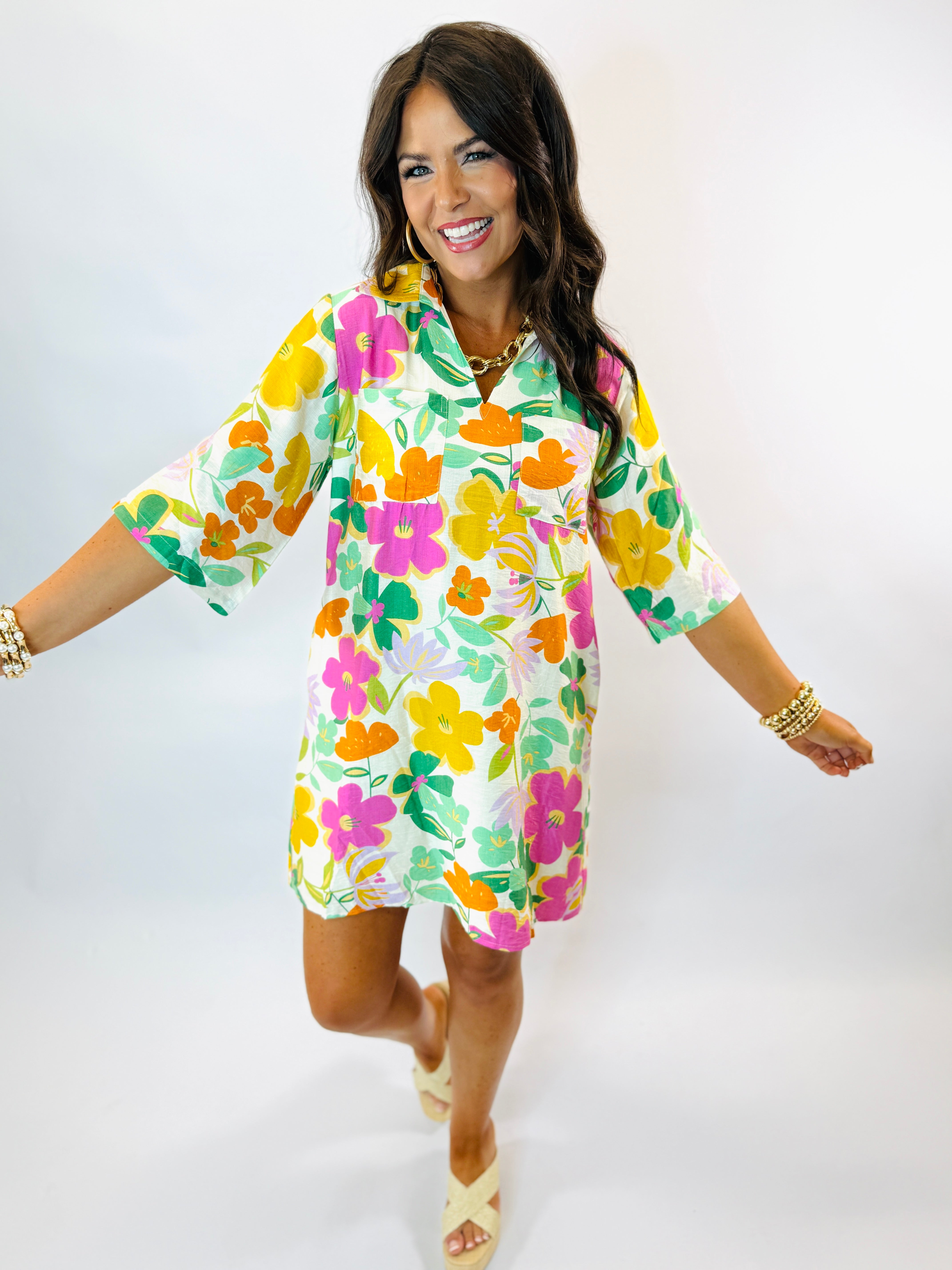 Woman wearing colorful floral print Gloria dress with short sleeves, featuring bright pink, yellow, orange and green flowe...