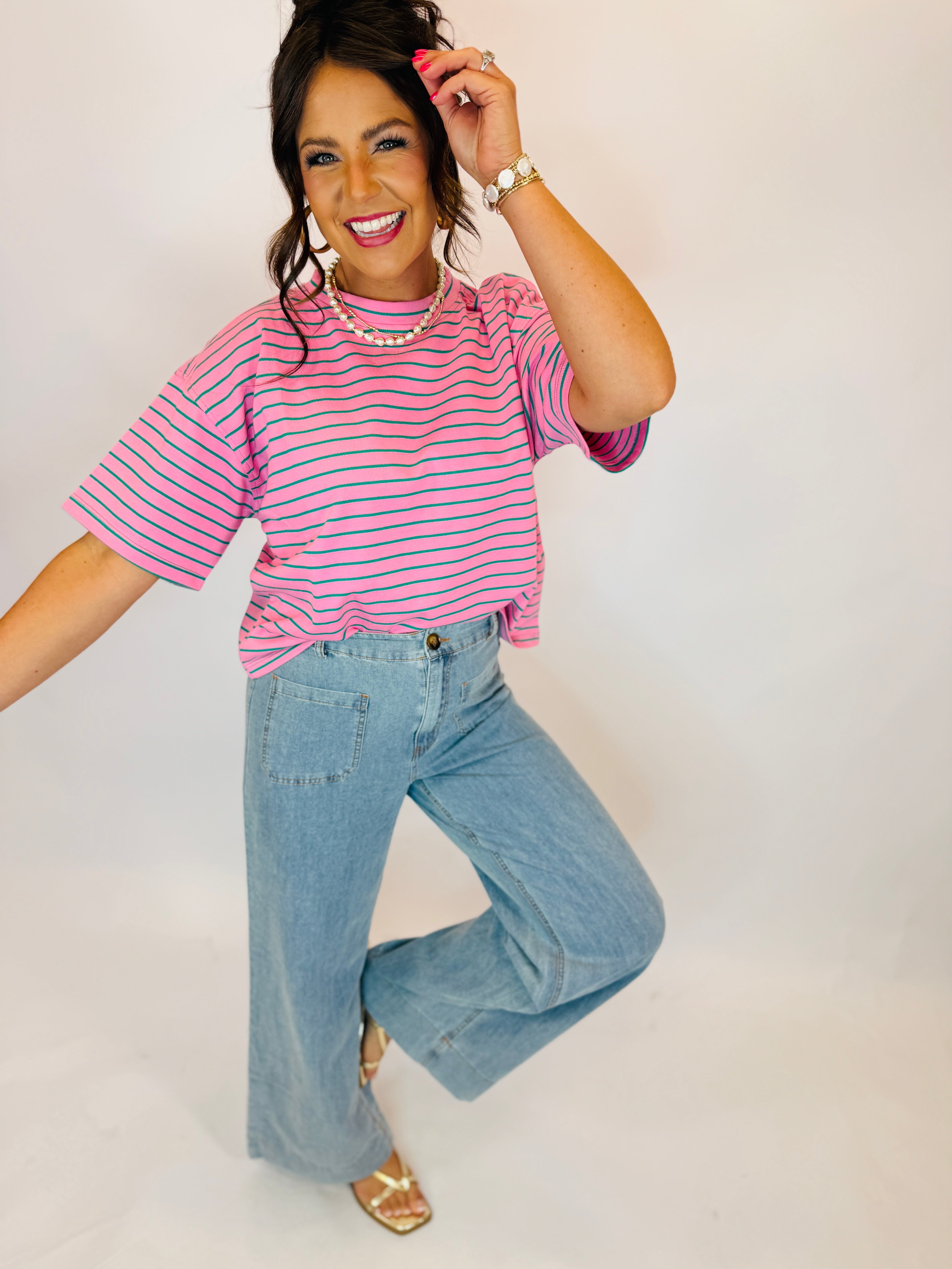 Wide-leg light wash denim jeans with front patch pockets, paired with pink striped top and gold sandals.