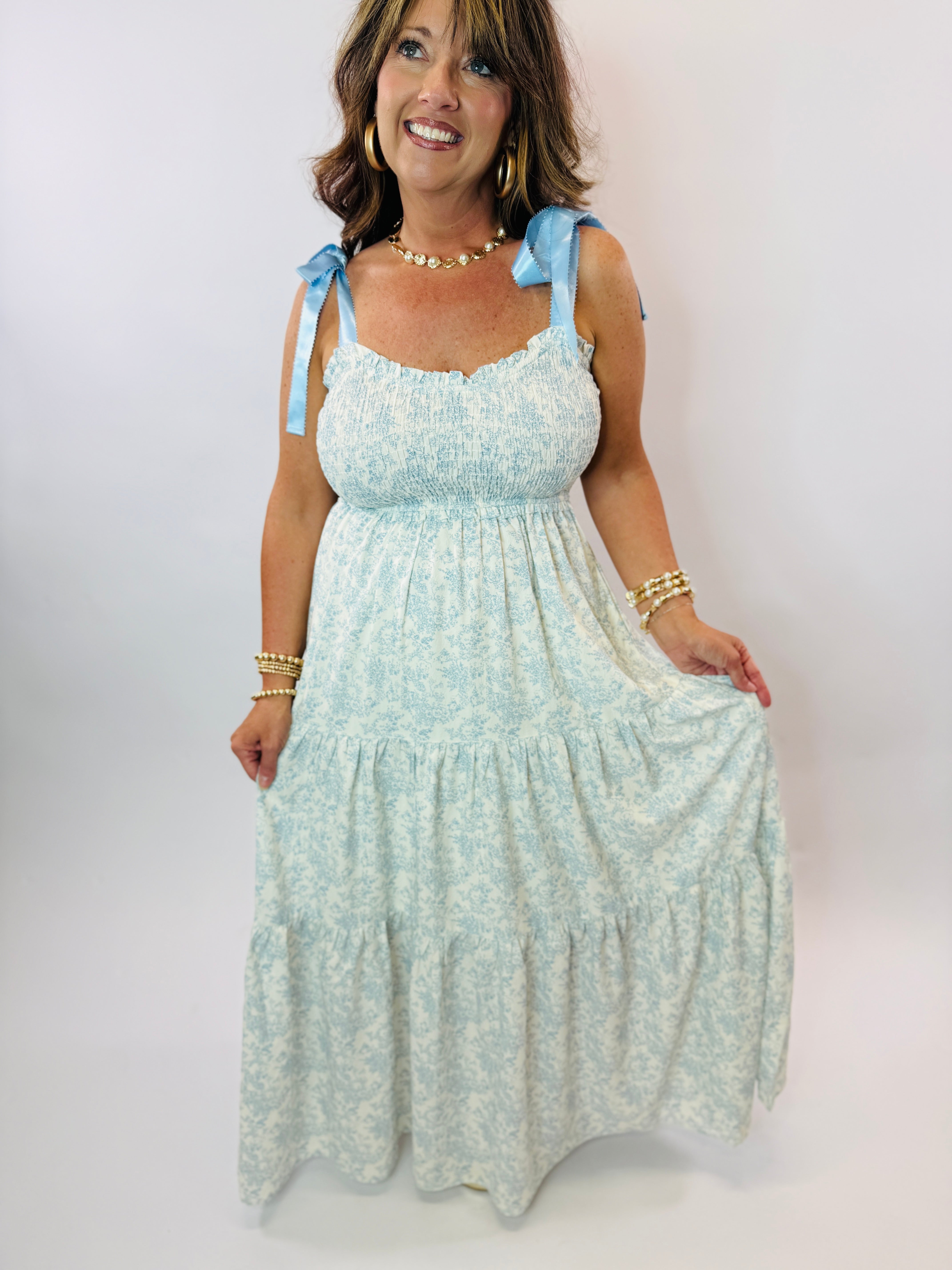 Woman wearing light blue floral maxi dress with smocked bodice, tie straps, and tiered ruffled skirt.