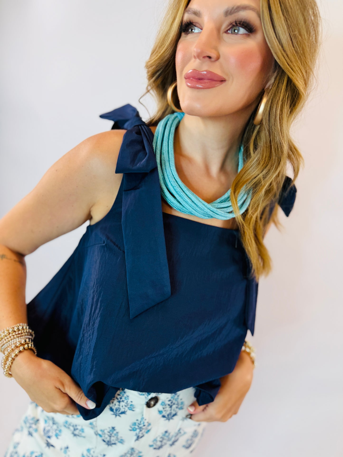 Woman wearing navy blue sleeveless top with shoulder bow detail and turquoise statement necklace.