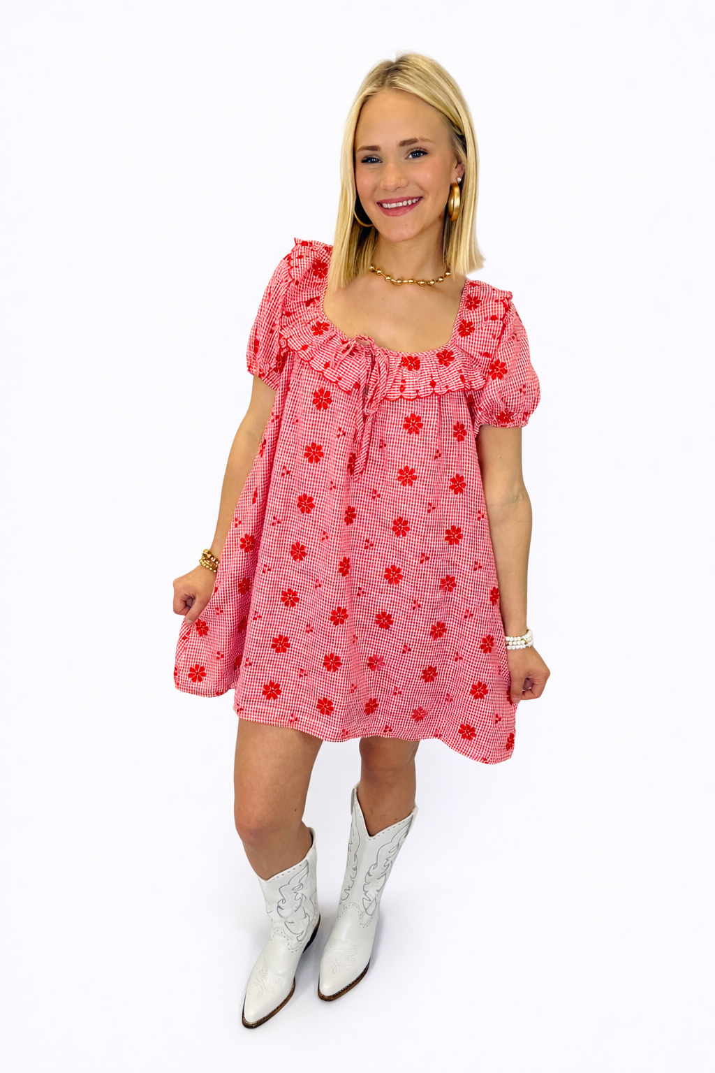 Woman wearing red gingham mini dress with floral embroidery, ruffled neckline, and white cowboy boots