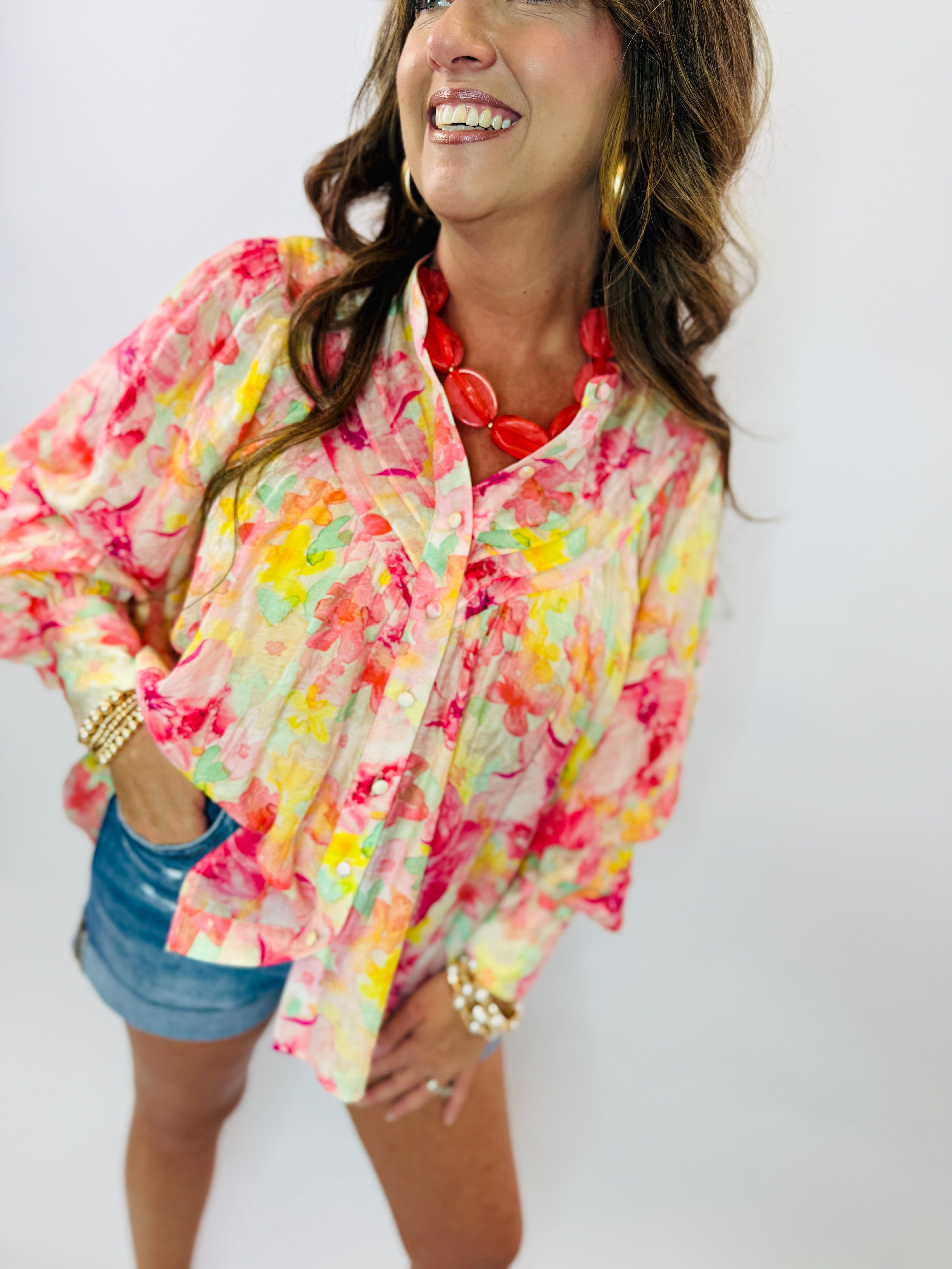 Woman wearing colorful floral print button-up shirt with vibrant pink, yellow, and green watercolor pattern