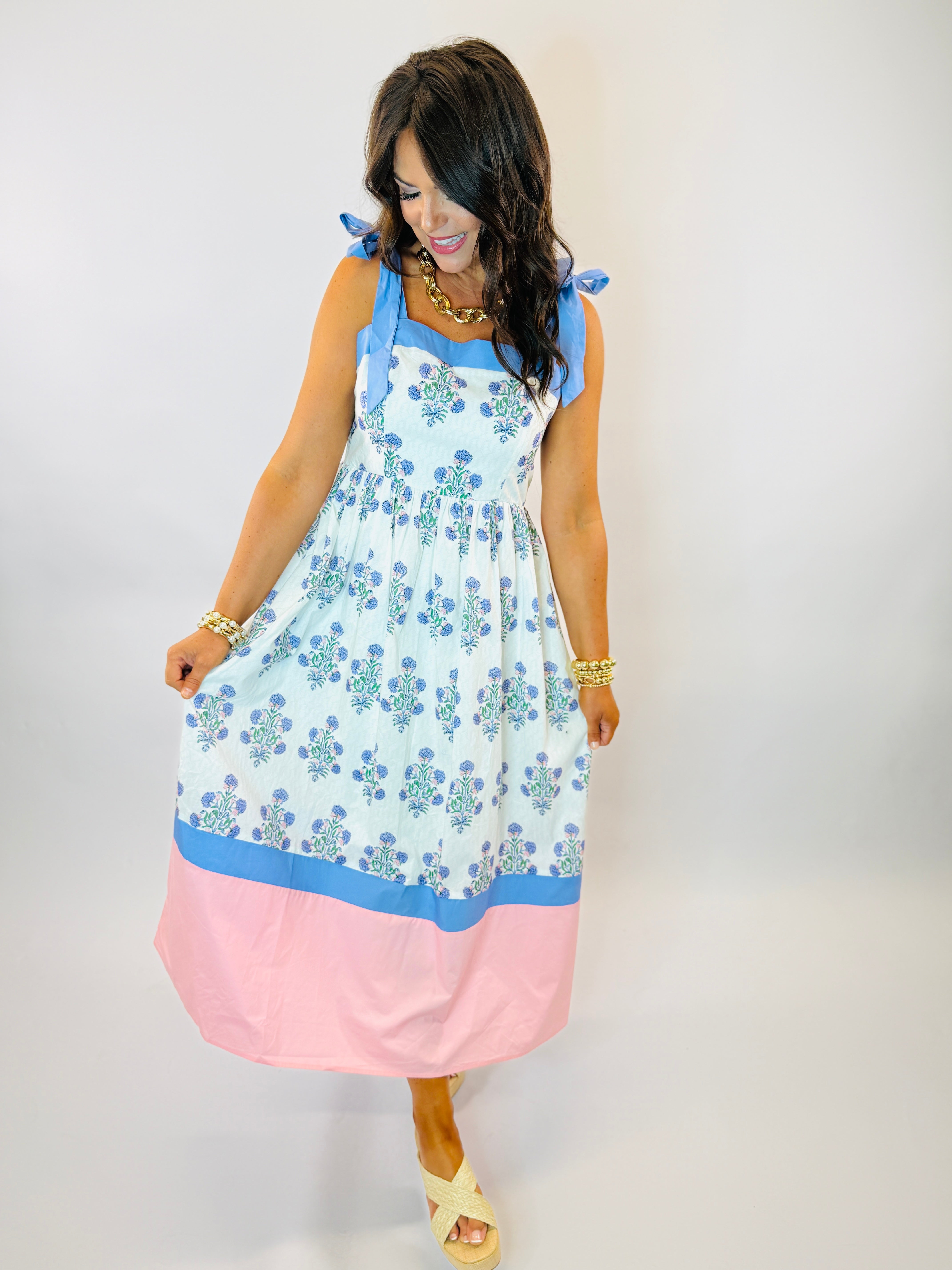 Woman wearing Jackie Dress with blue floral print bodice, pink color block hem, and blue tie shoulder straps.