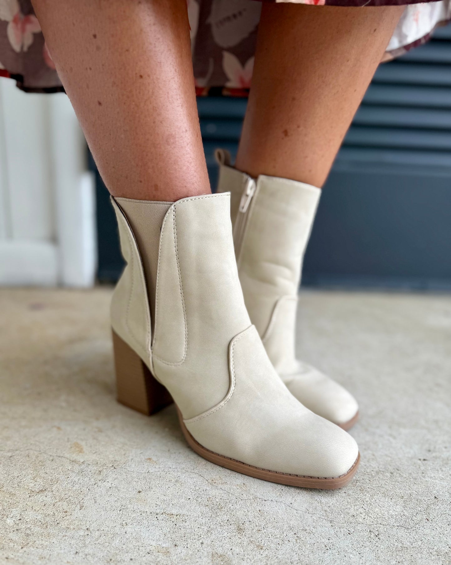 Cream-colored ankle boots with elastic side panels and block heels, worn on person's legs