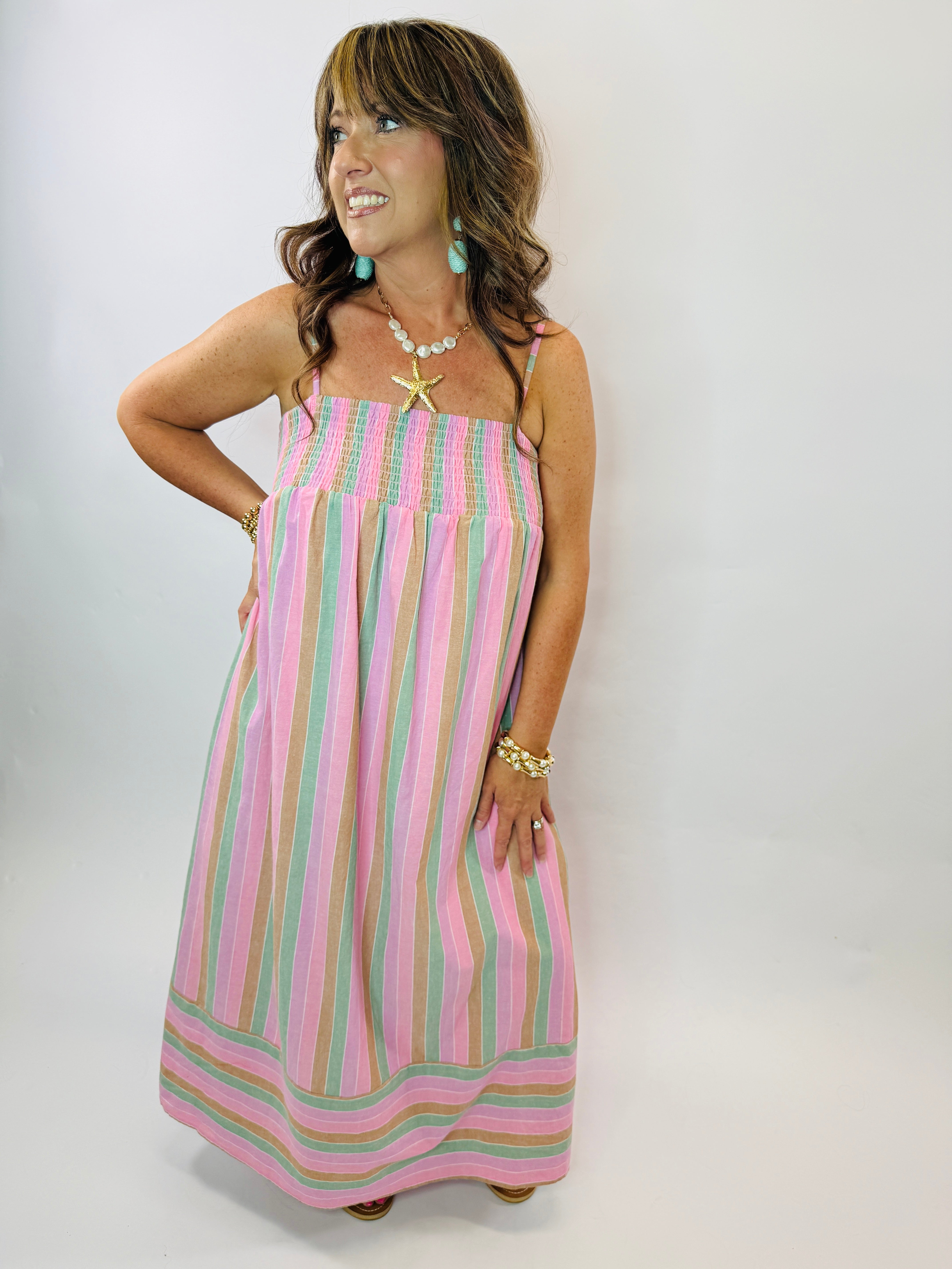 Woman wearing colorful striped maxi dress with pink, green, and beige vertical stripes and smocked bodice