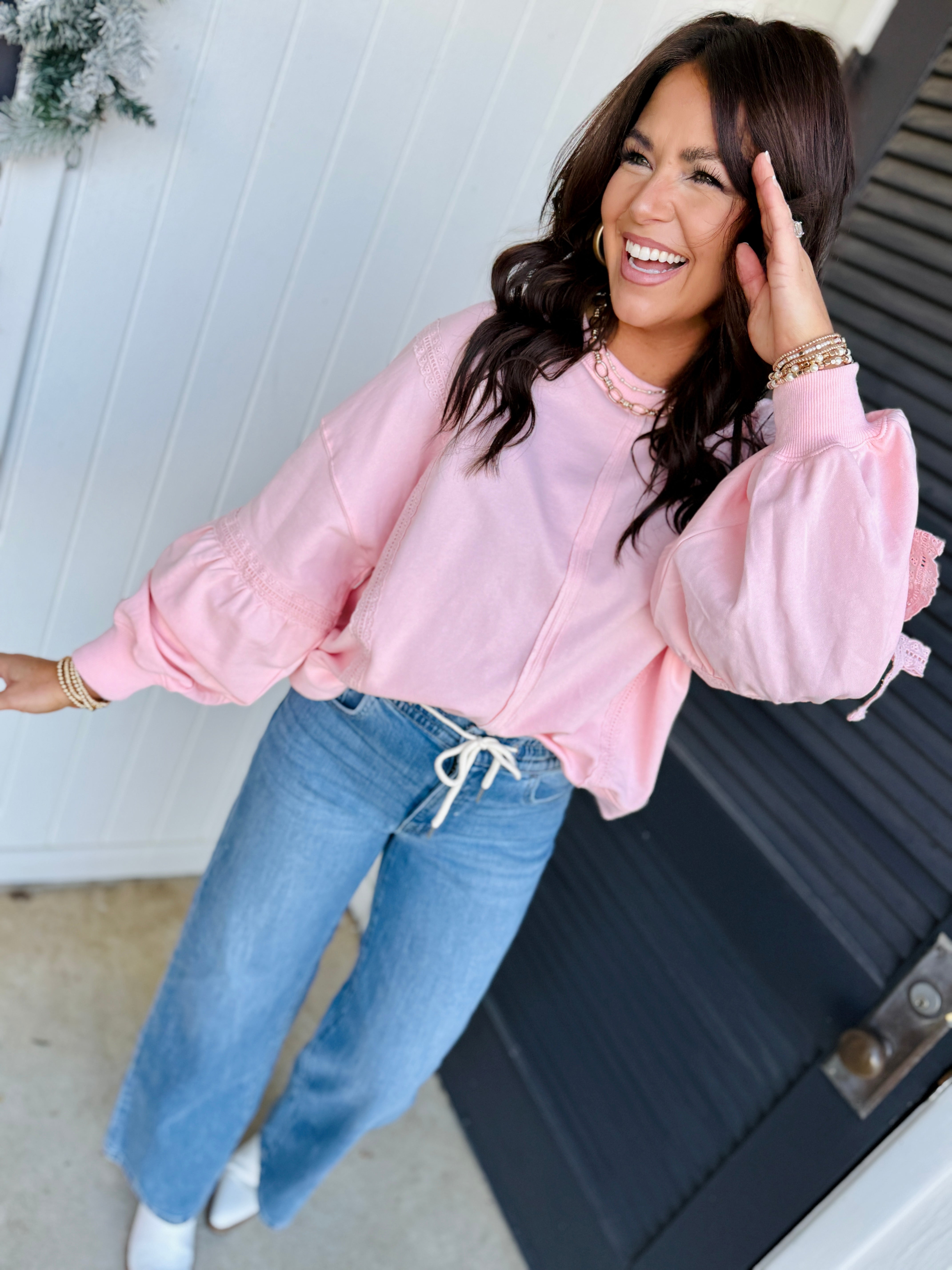 Woman wearing light wash blue denim jeans with drawstring waist and pink sweatshirt, smiling outdoors.