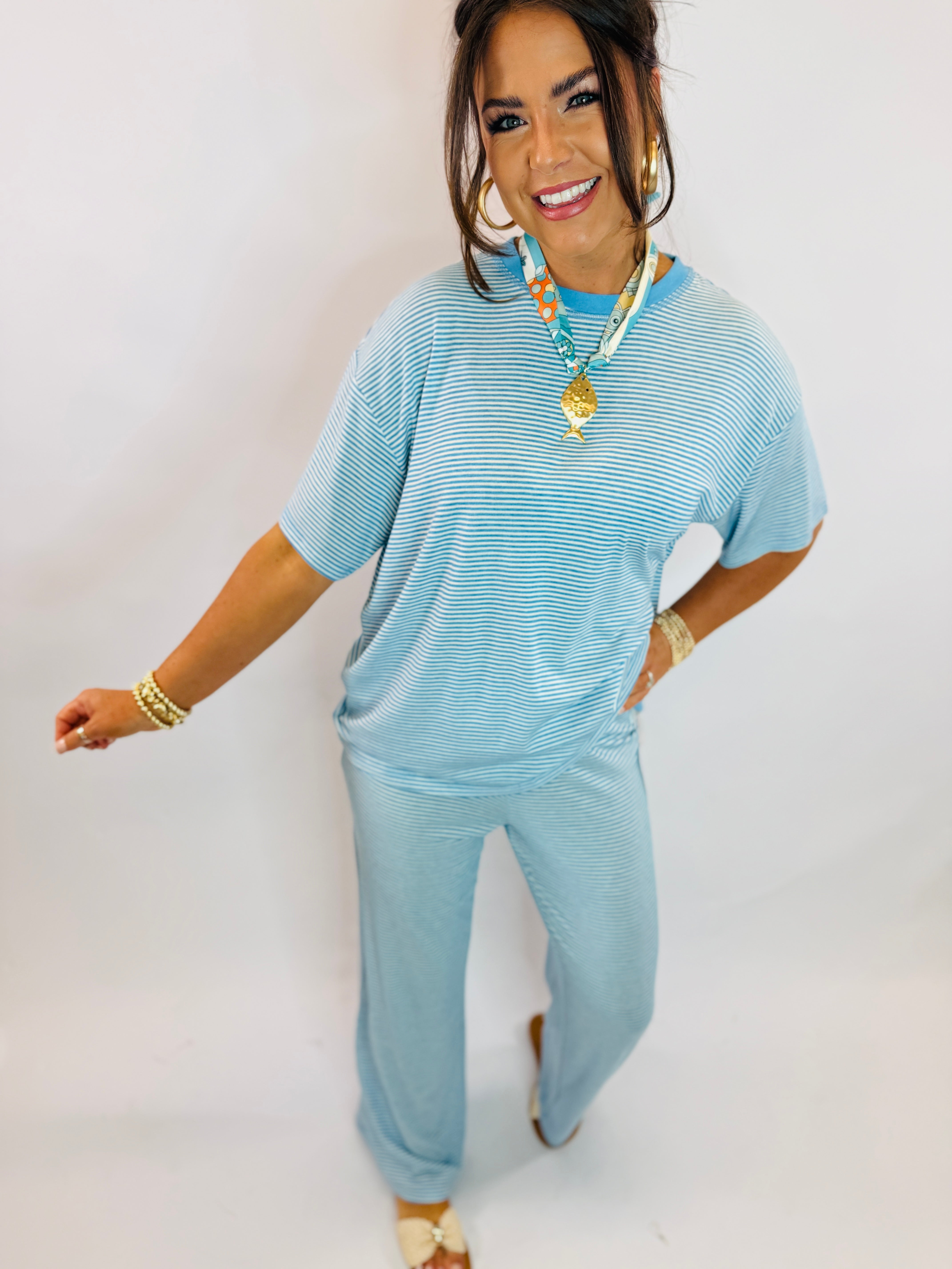 Woman wearing light blue ribbed short-sleeve top and matching wide-leg pants, styled with gold jewelry and colorful necklace.