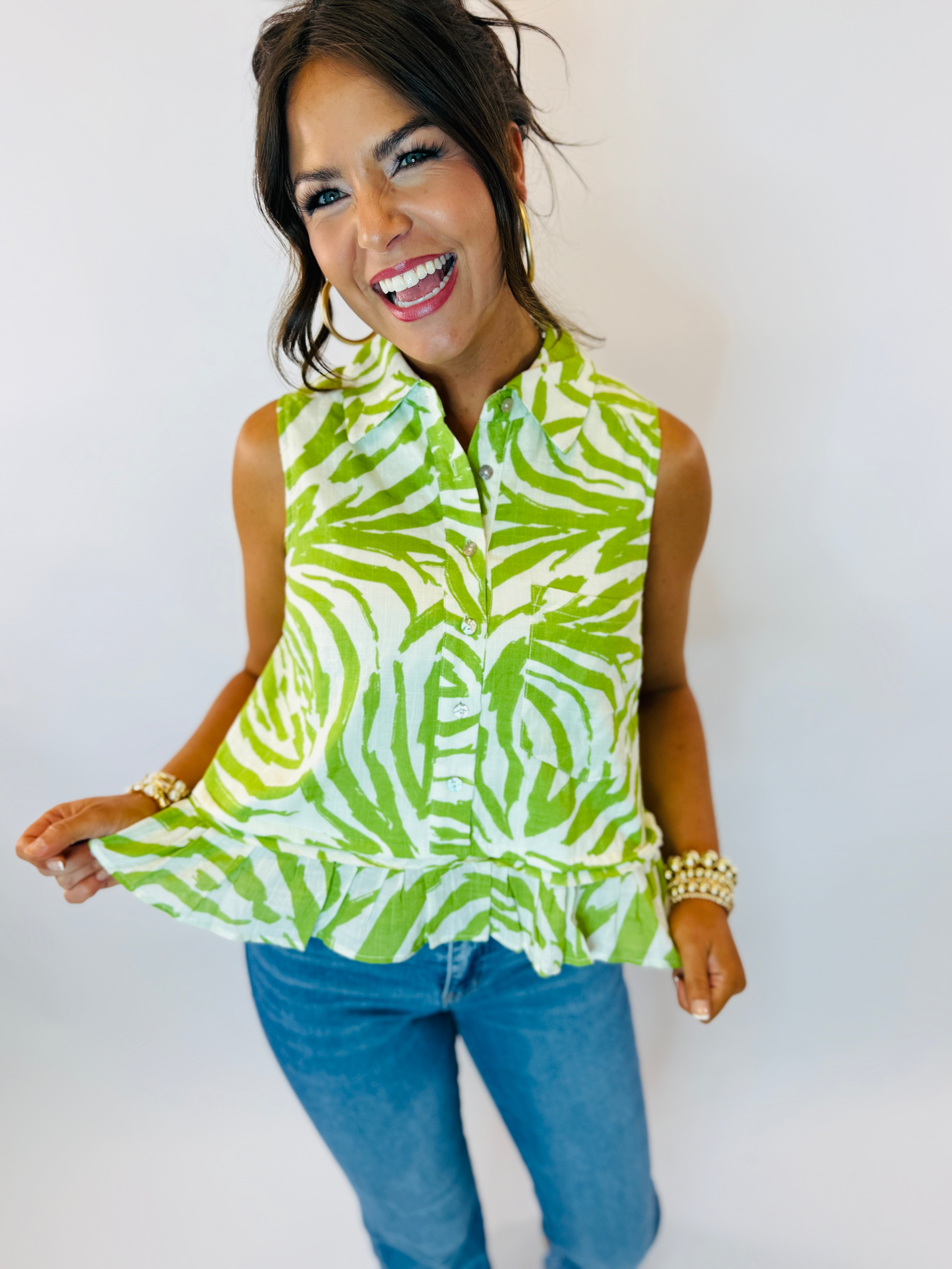 Woman wearing sleeveless green and white zebra print button-up blouse with blue jeans and pearl bracelet