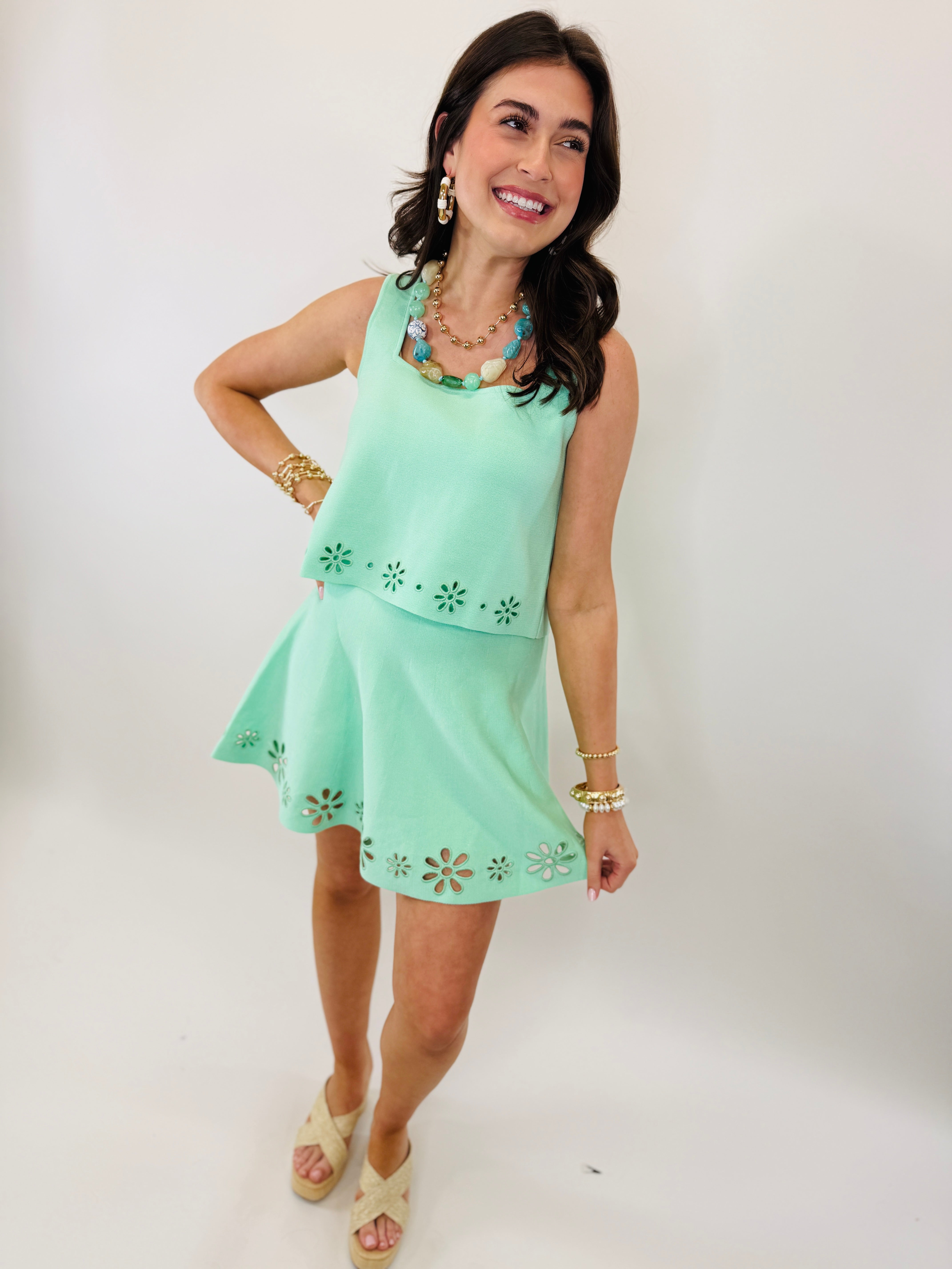 Woman wearing mint green two-piece set with laser-cut floral details, paired with gold jewelry and wedge sandals.