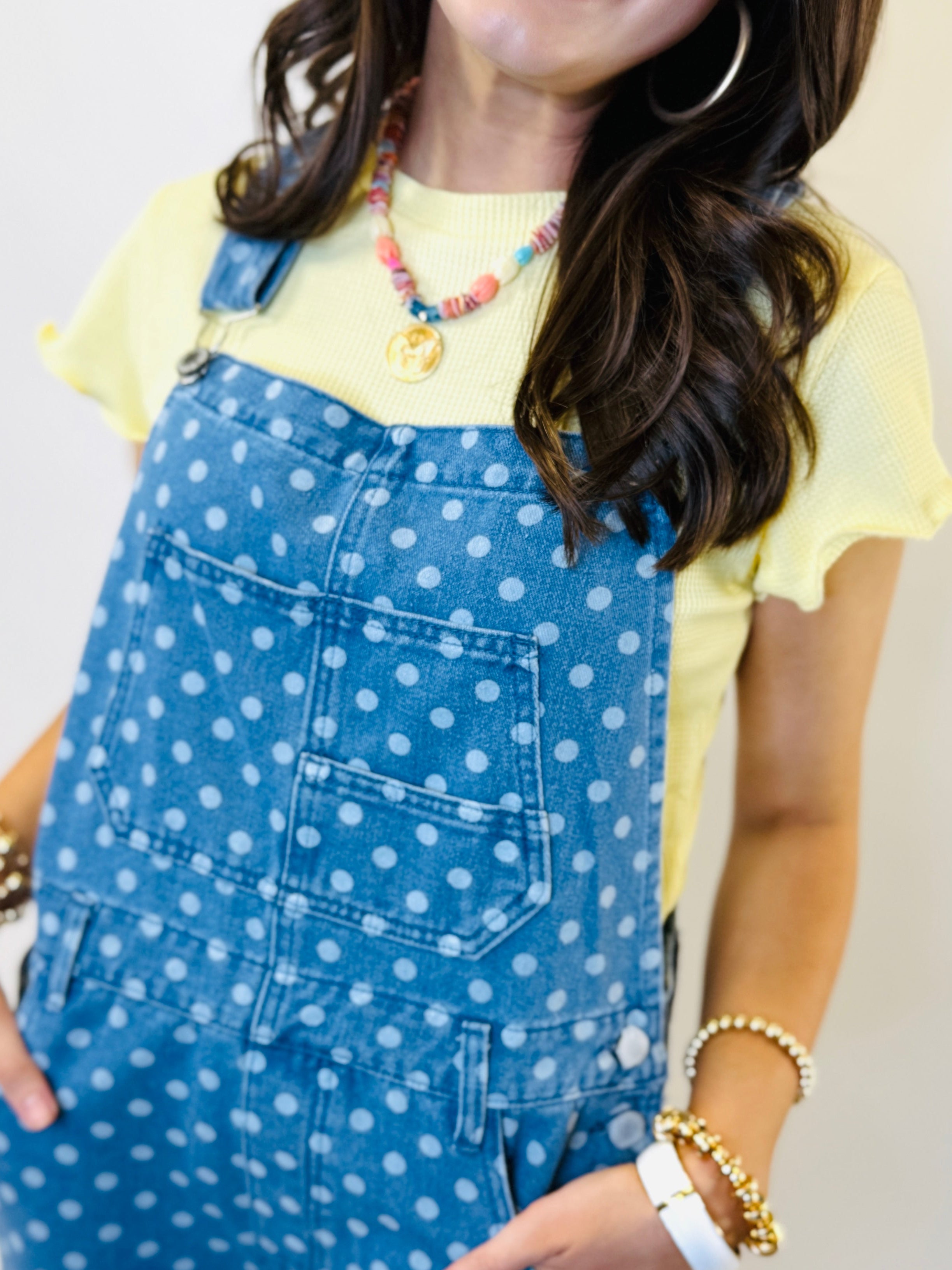 Woman wearing blue polka dot denim overalls with yellow t-shirt and colorful beaded necklace