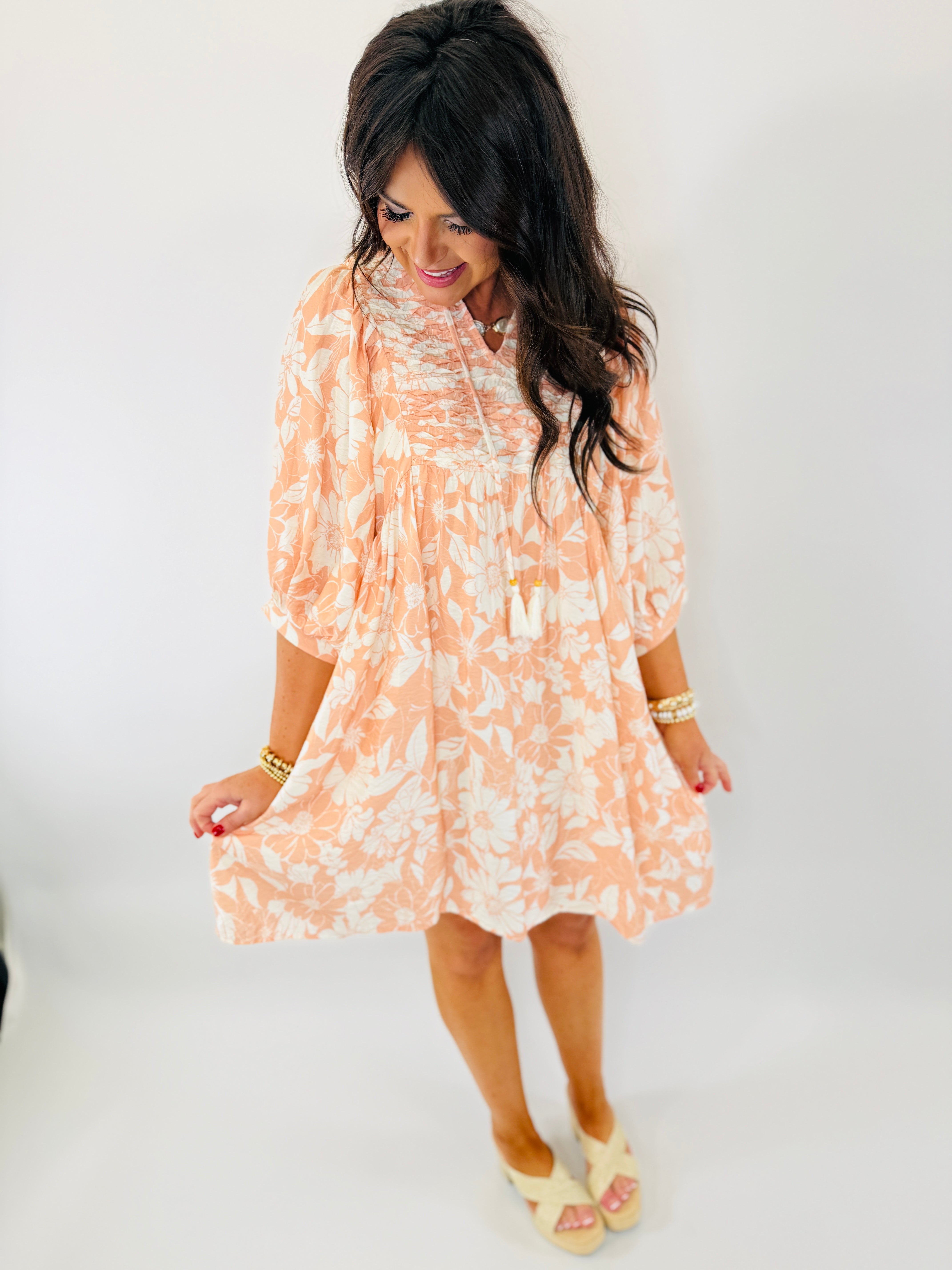 Woman wearing coral and white floral print Rebecca dress with three-quarter sleeves and tiered ruffle hem.