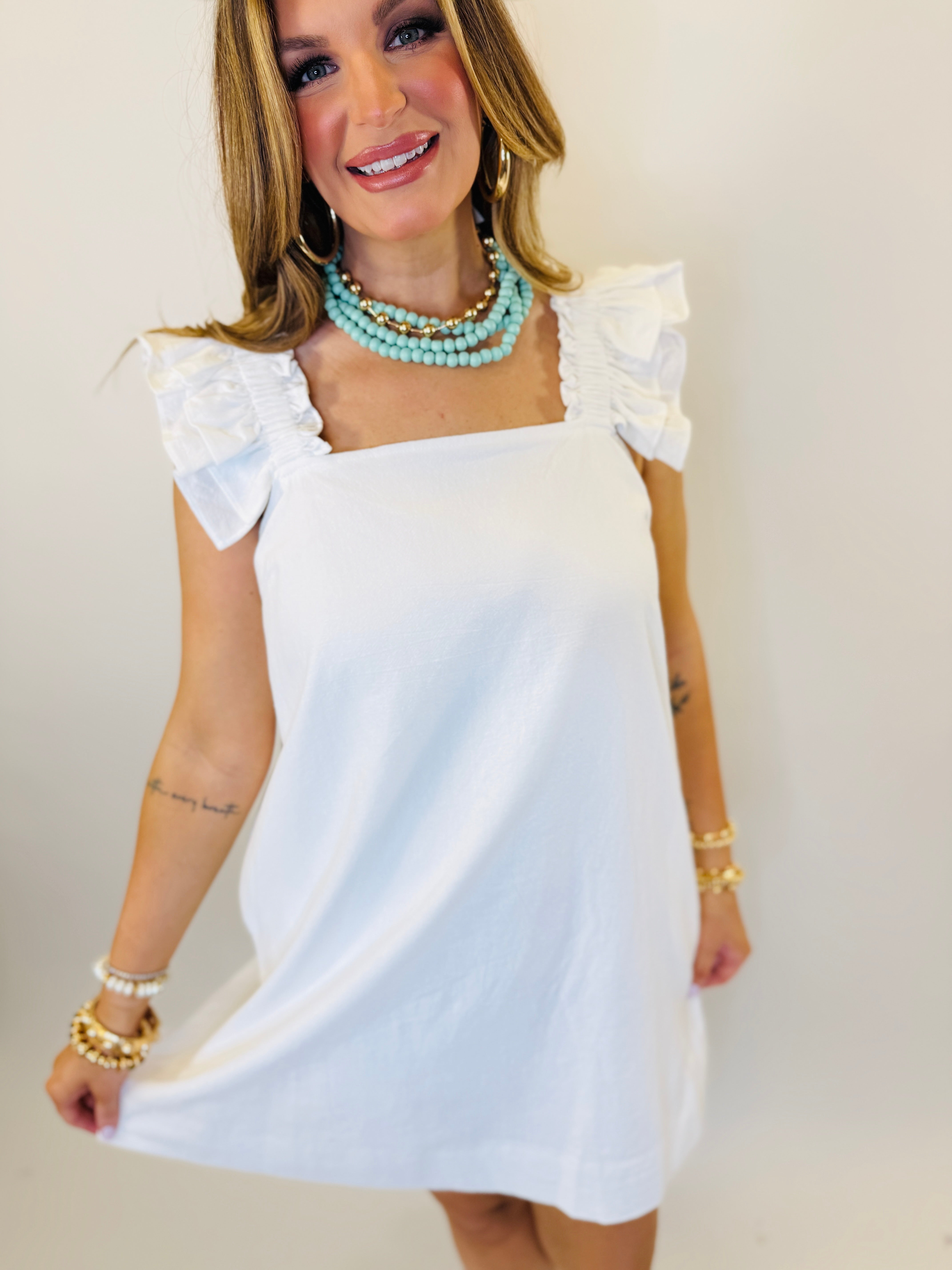 White ruffle sleeve mini dress with square neckline modeled with turquoise beaded necklace and pearl bracelets