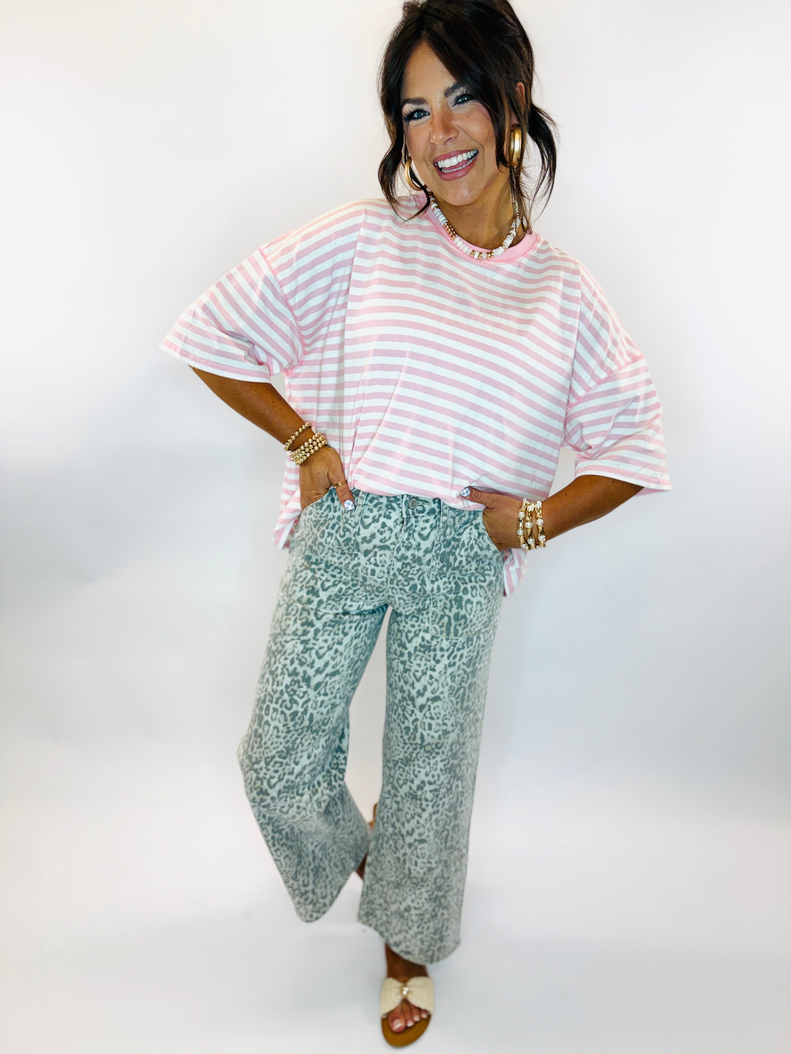 Woman wearing pink striped oversized t-shirt and sage green leopard print wide-leg denim jeans with gold jewelry accessories.