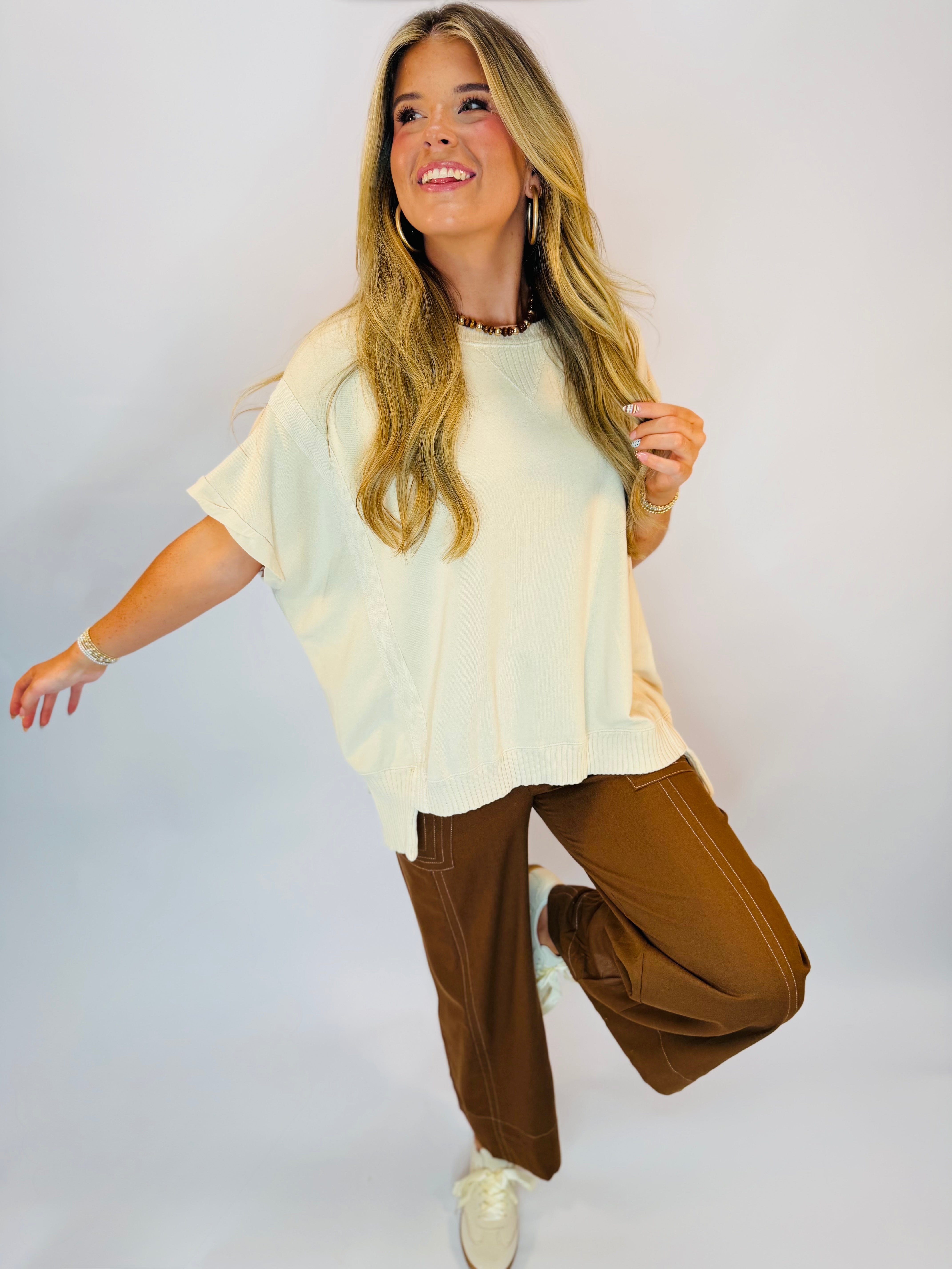 Cream short-sleeve oversized knit top with ribbed hem, styled with brown wide-leg pants.