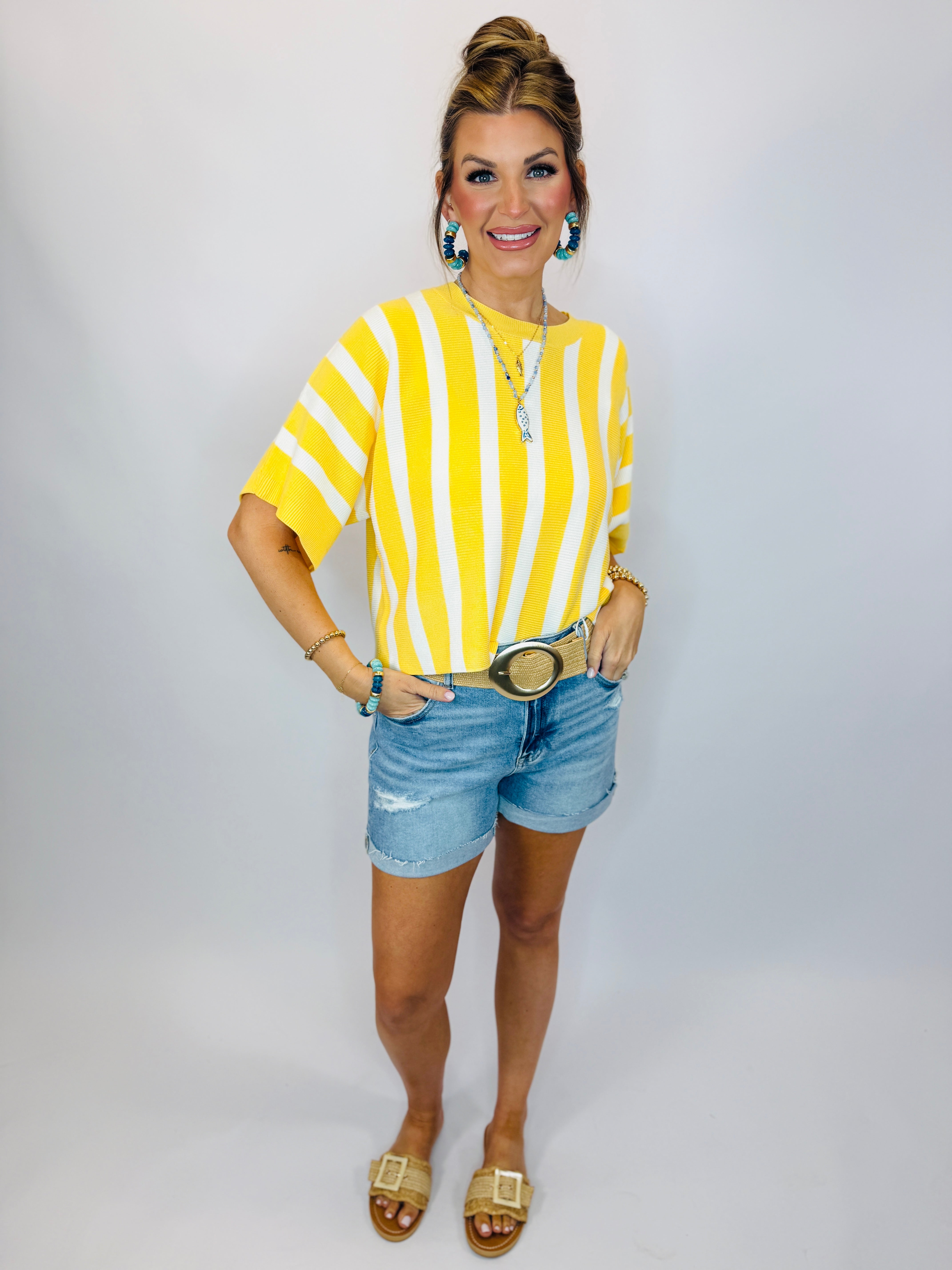 Woman wearing yellow and white striped oversized top with denim shorts and turquoise earrings