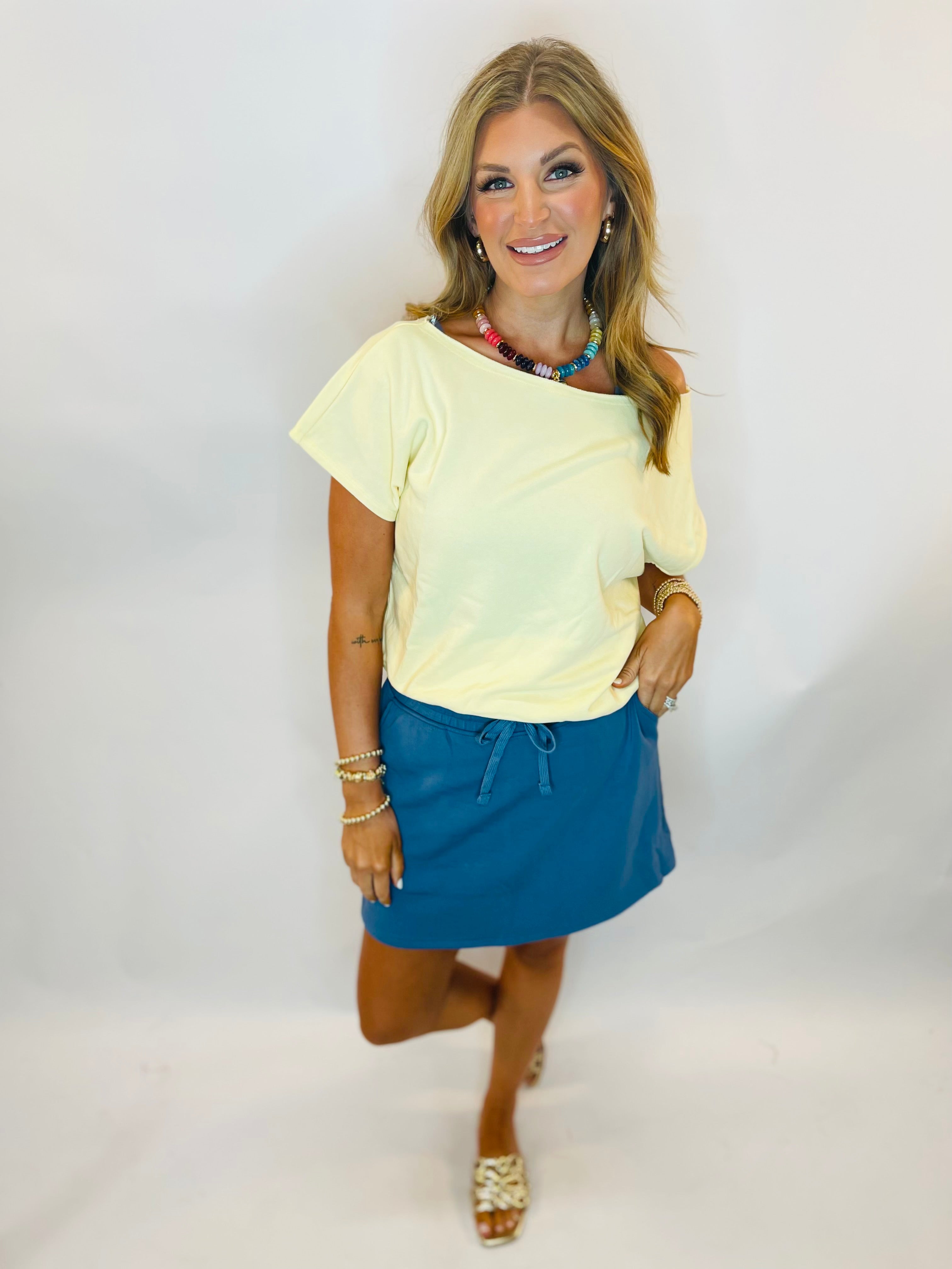 Woman wearing a pale yellow asymmetric one-shoulder short-sleeve top paired with a teal mini skirt.