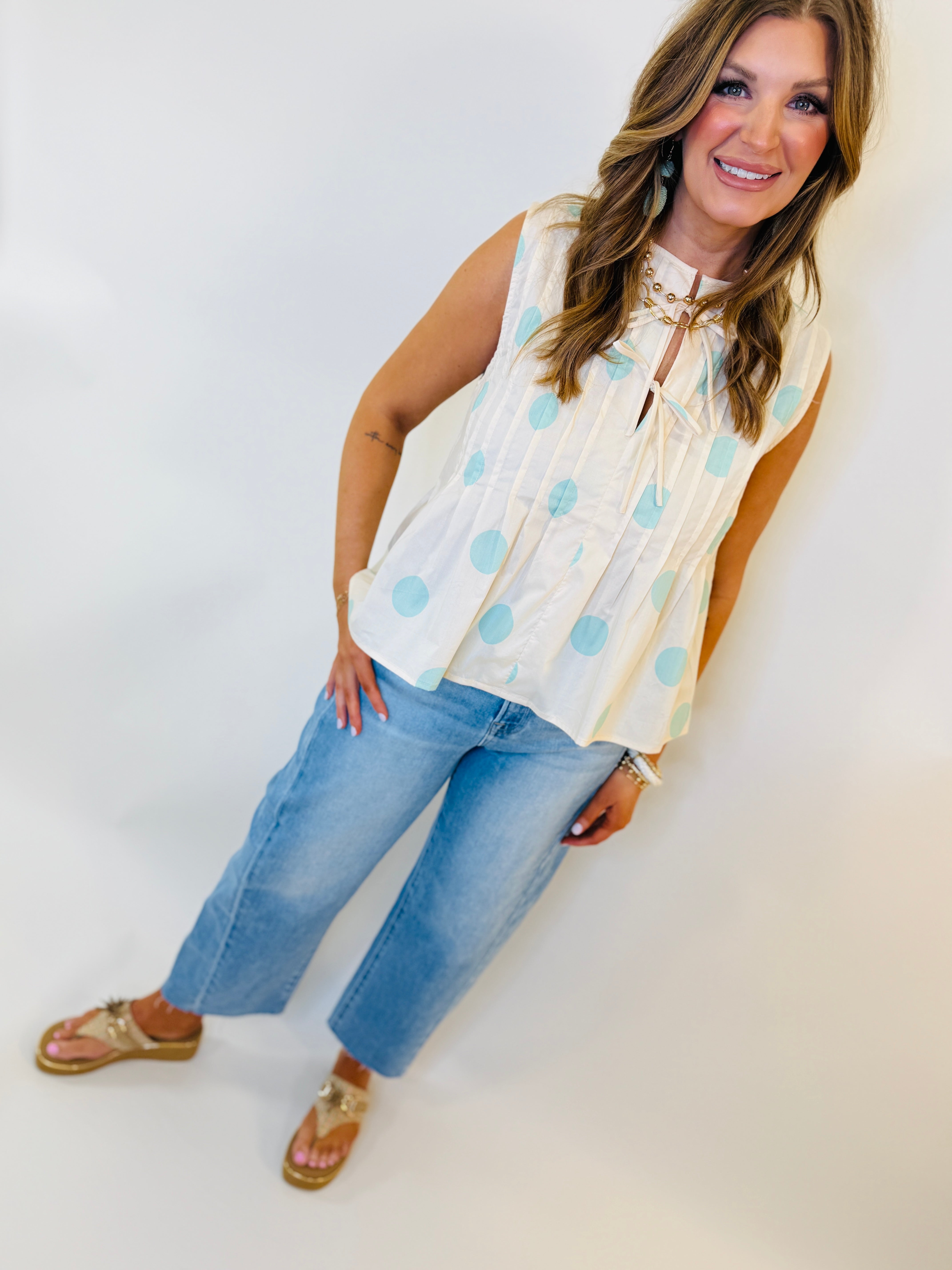 Woman wearing white sleeveless polka dot blouse with tie neck detail and blue jeans