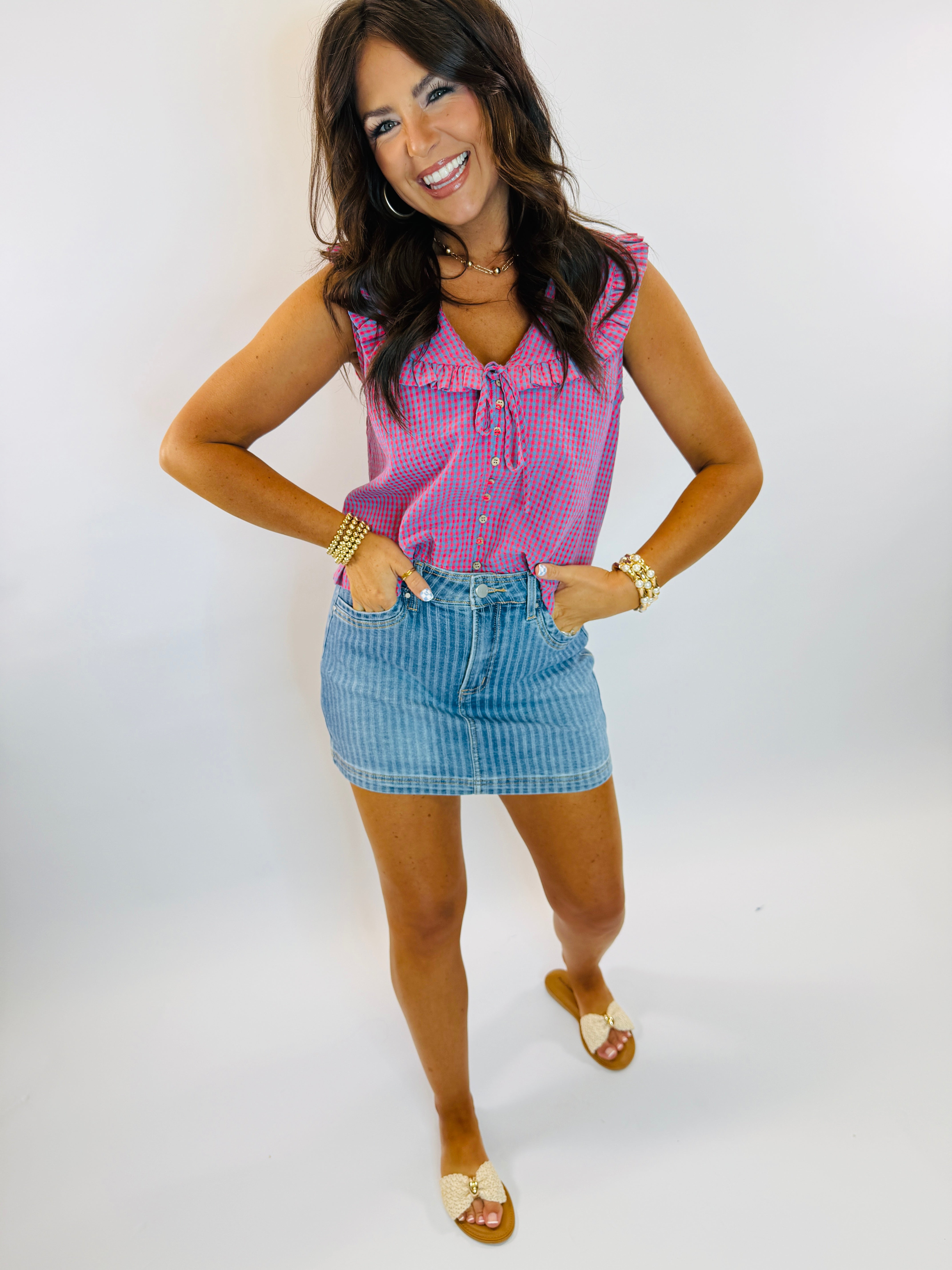 Woman wearing pink gingham sleeveless ruffle tank top with lace-up neckline, paired with denim skirt