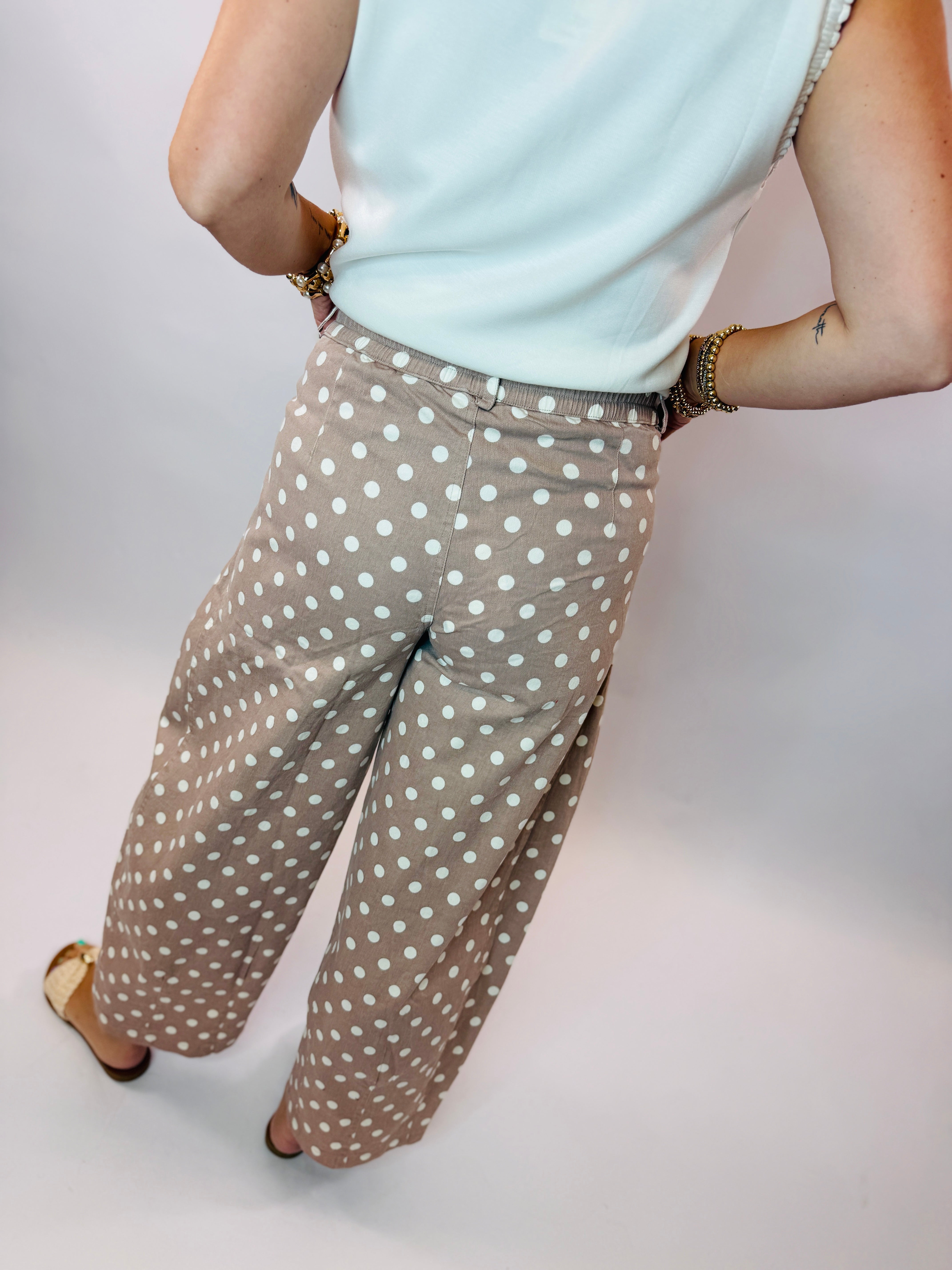 Woman wearing beige polka dot wide-leg barrel pants with light blue top and gold accessories.