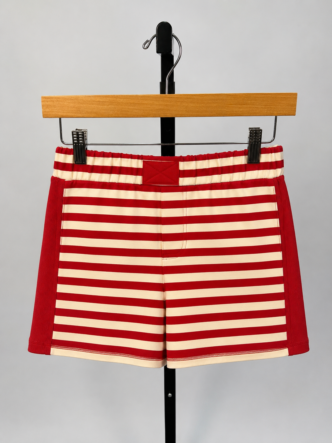Red and cream striped knit shorts with ribbed side panels hanging on wooden hanger