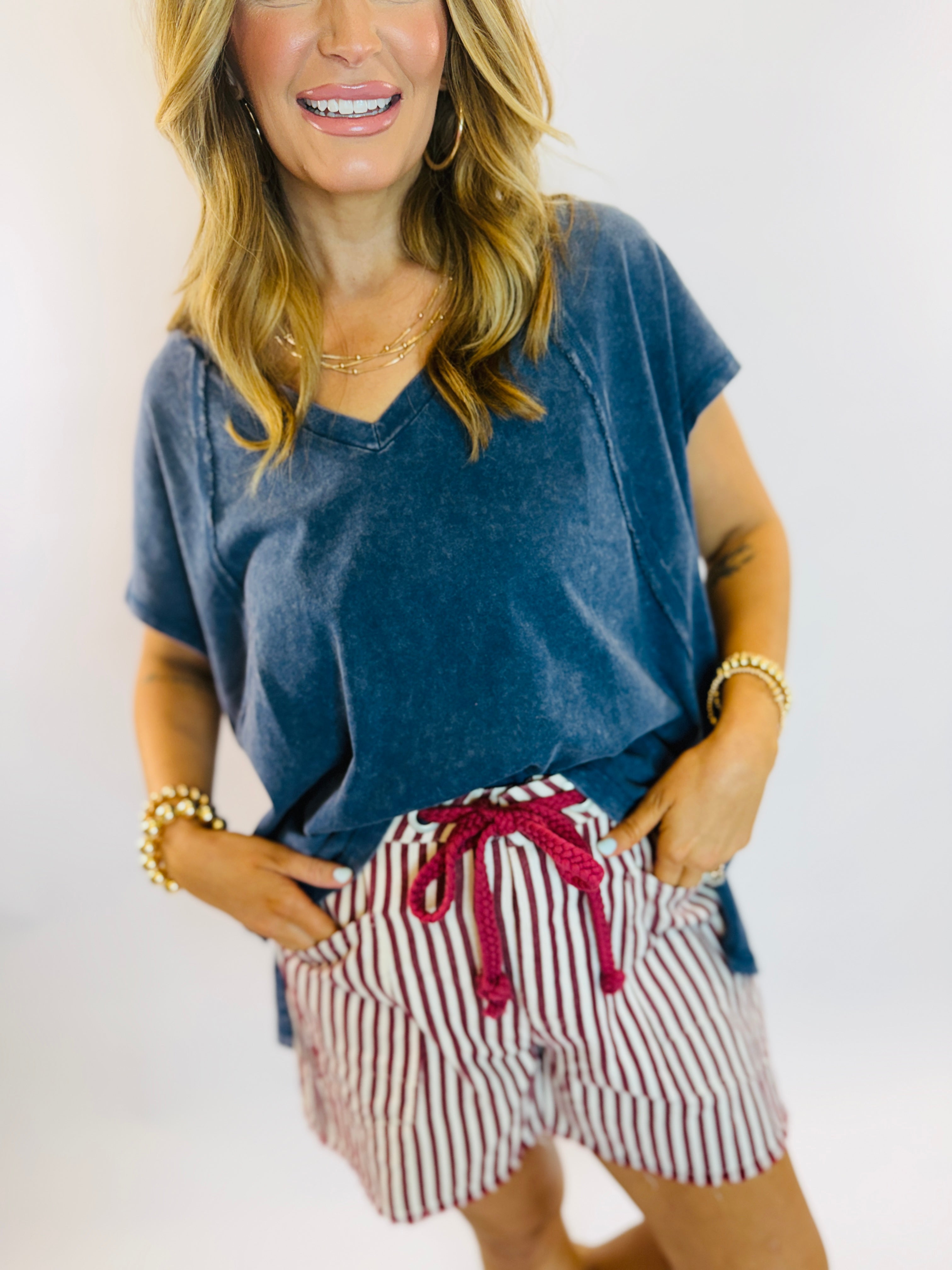 Woman wearing blue oversized v-neck tee with red and white striped drawstring shorts, gold jewelry accessories.