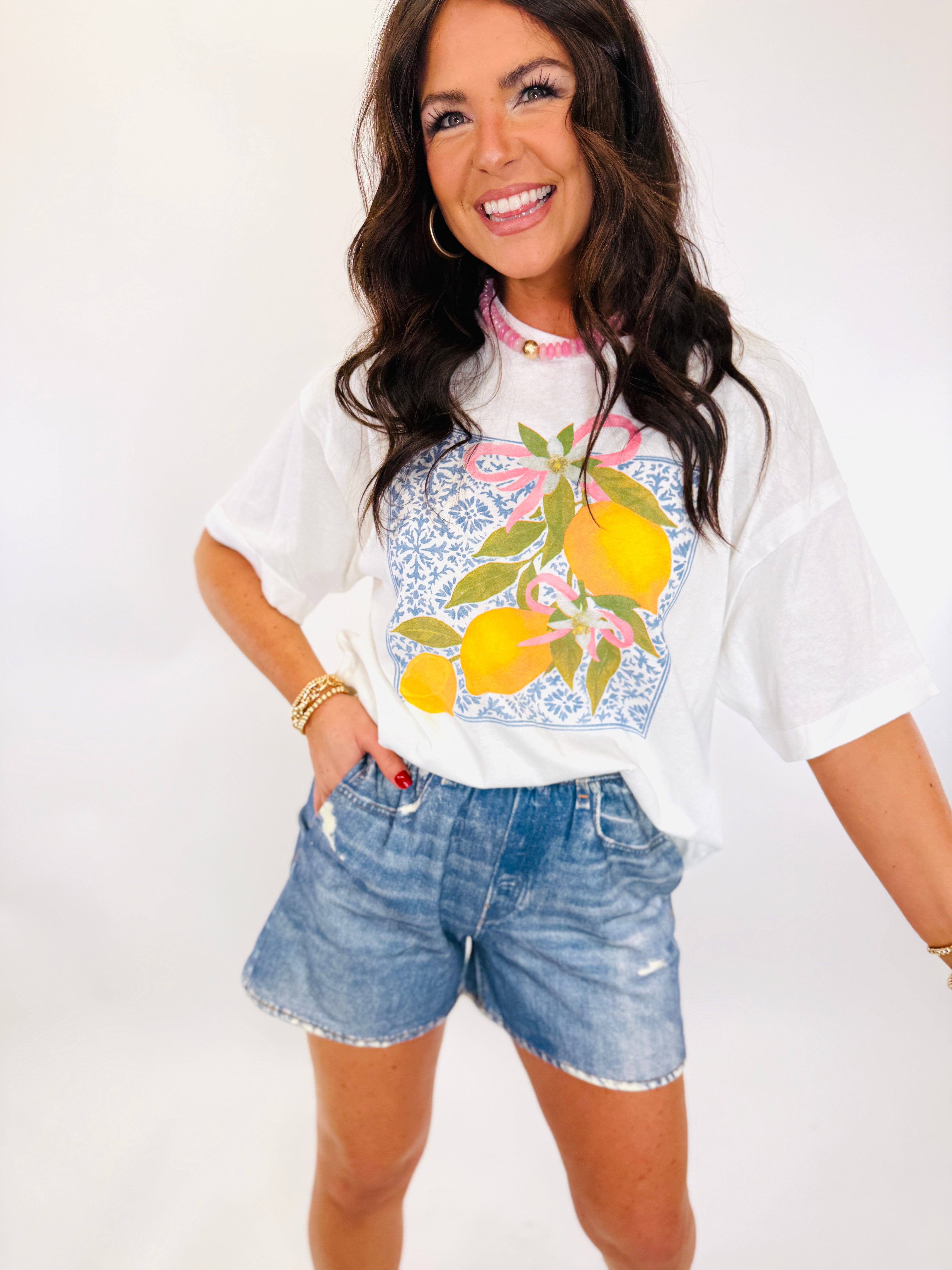 Woman wearing white lemon-print t-shirt and light blue distressed denim shorts in casual summer outfit.