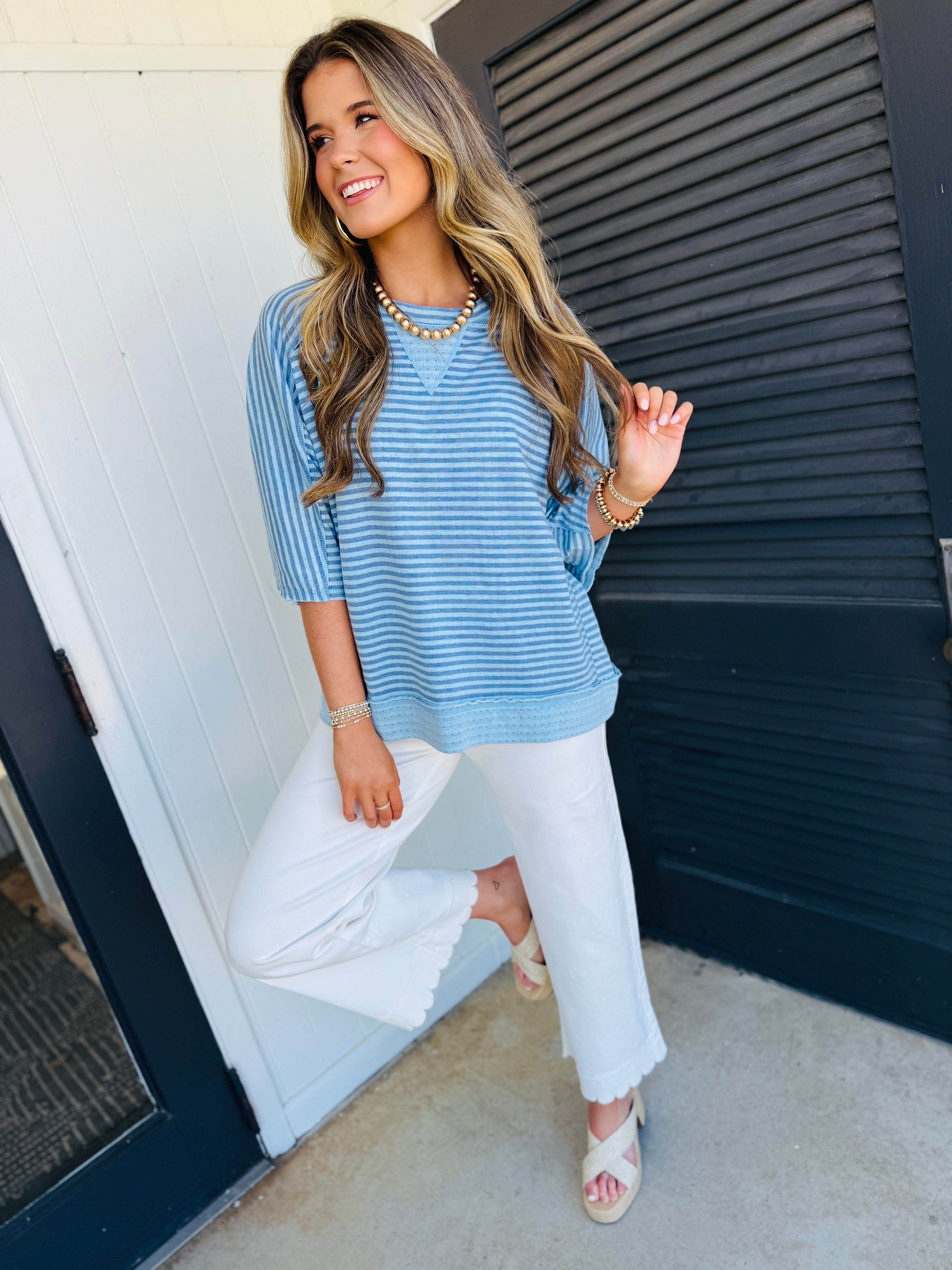 Woman wearing blue and white striped cozy pullover top with white jeans and gold jewelry accessories.
