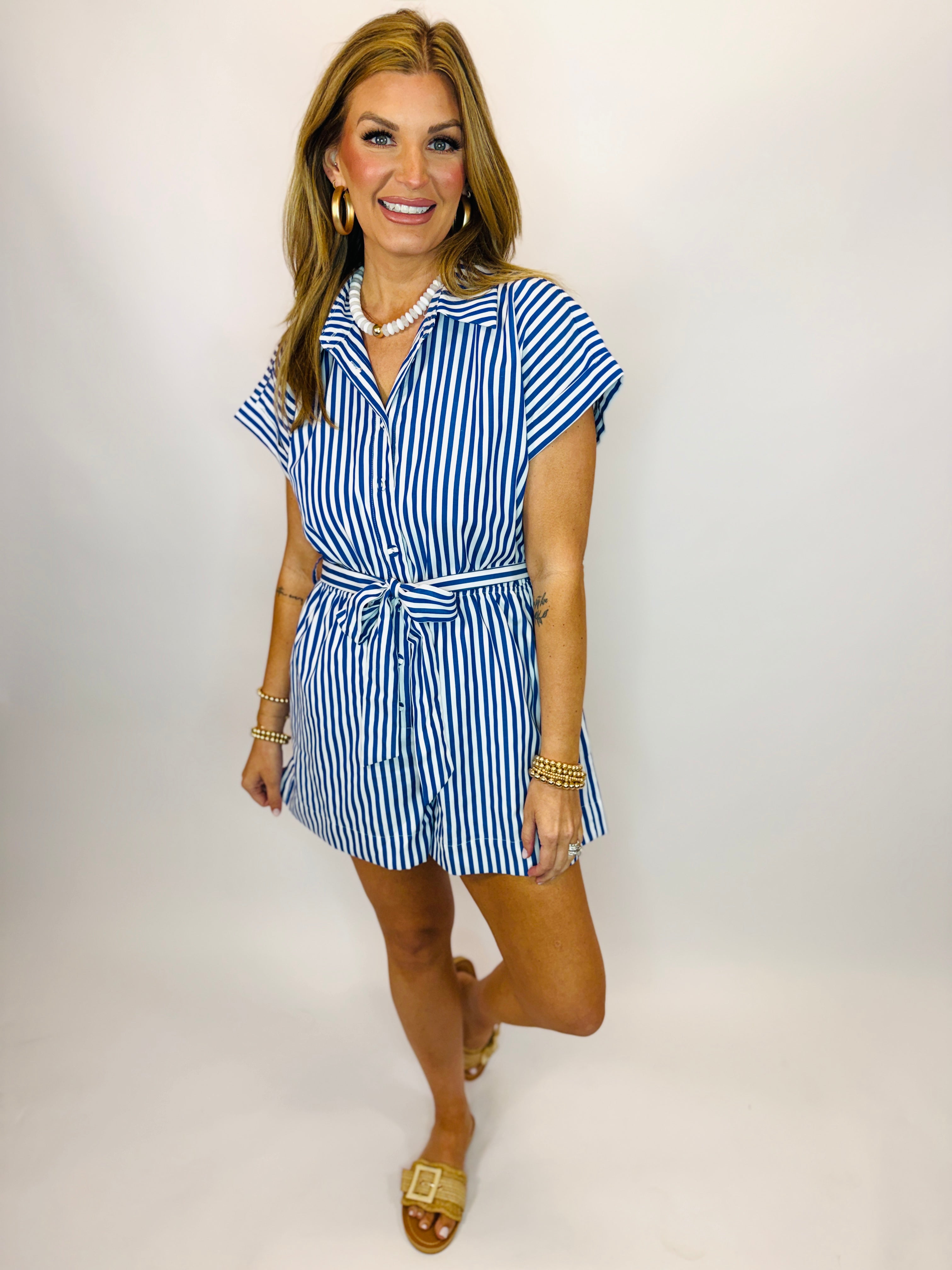 Woman wearing blue and white striped short-sleeve romper with tie belt and button-front closure