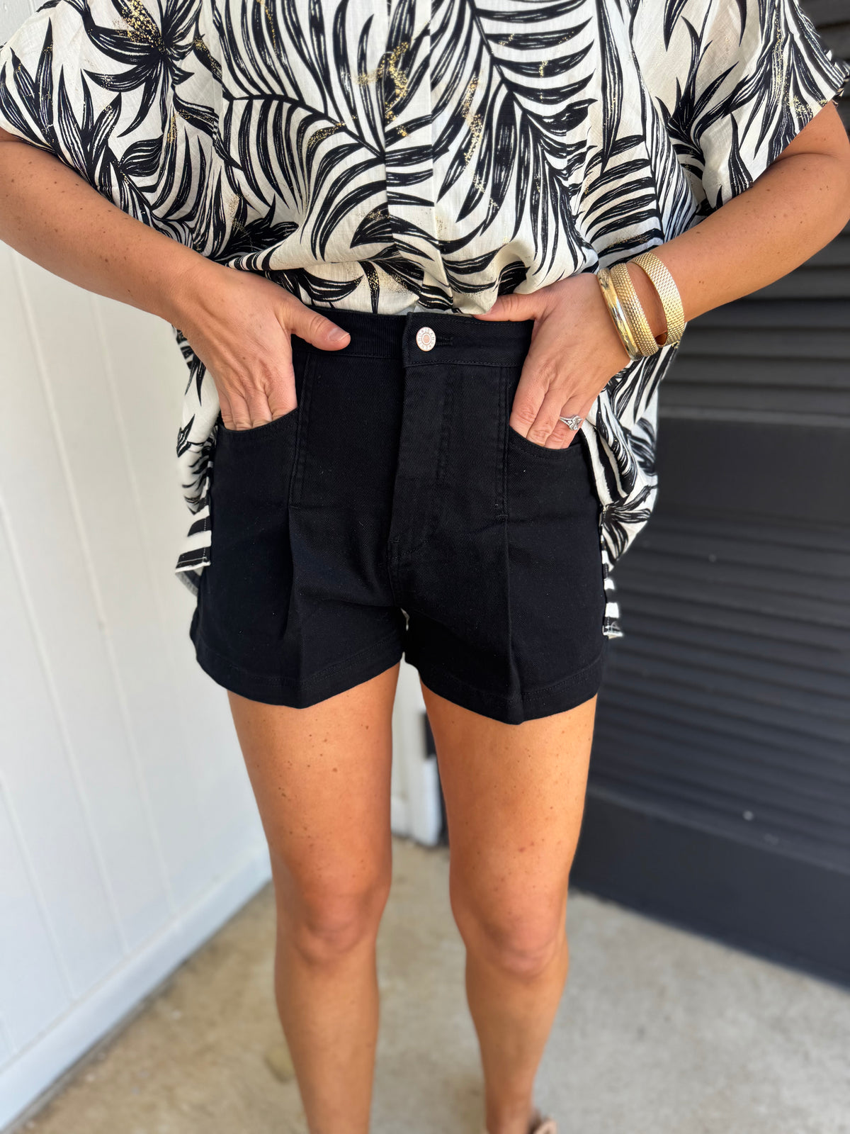 Woman wearing black high-waisted Loretta shorts with hands in pockets, paired with tropical print top