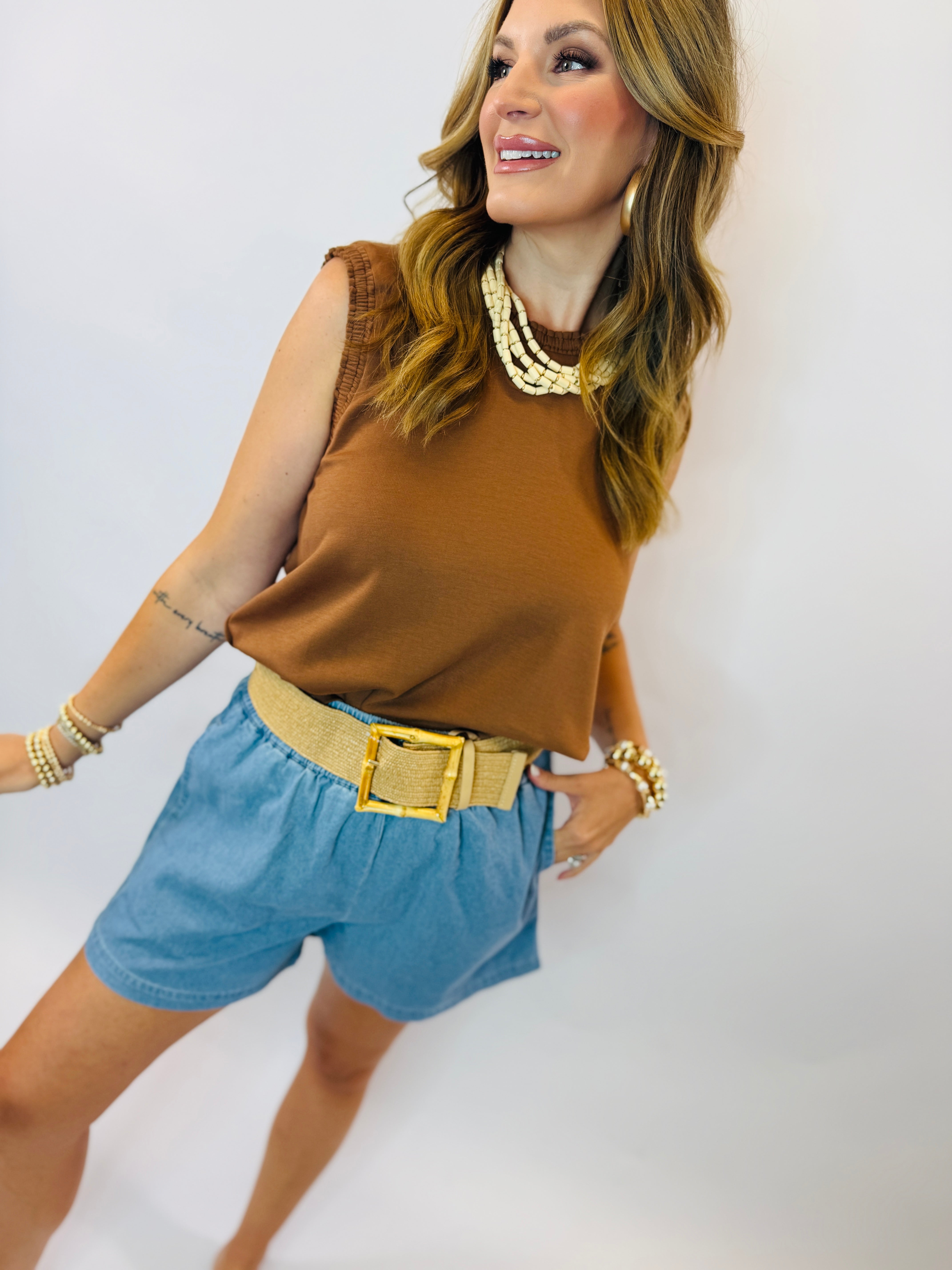 Woman wearing brown sleeveless top and blue Joni pull-on shorts with tan belt and pearl necklace.