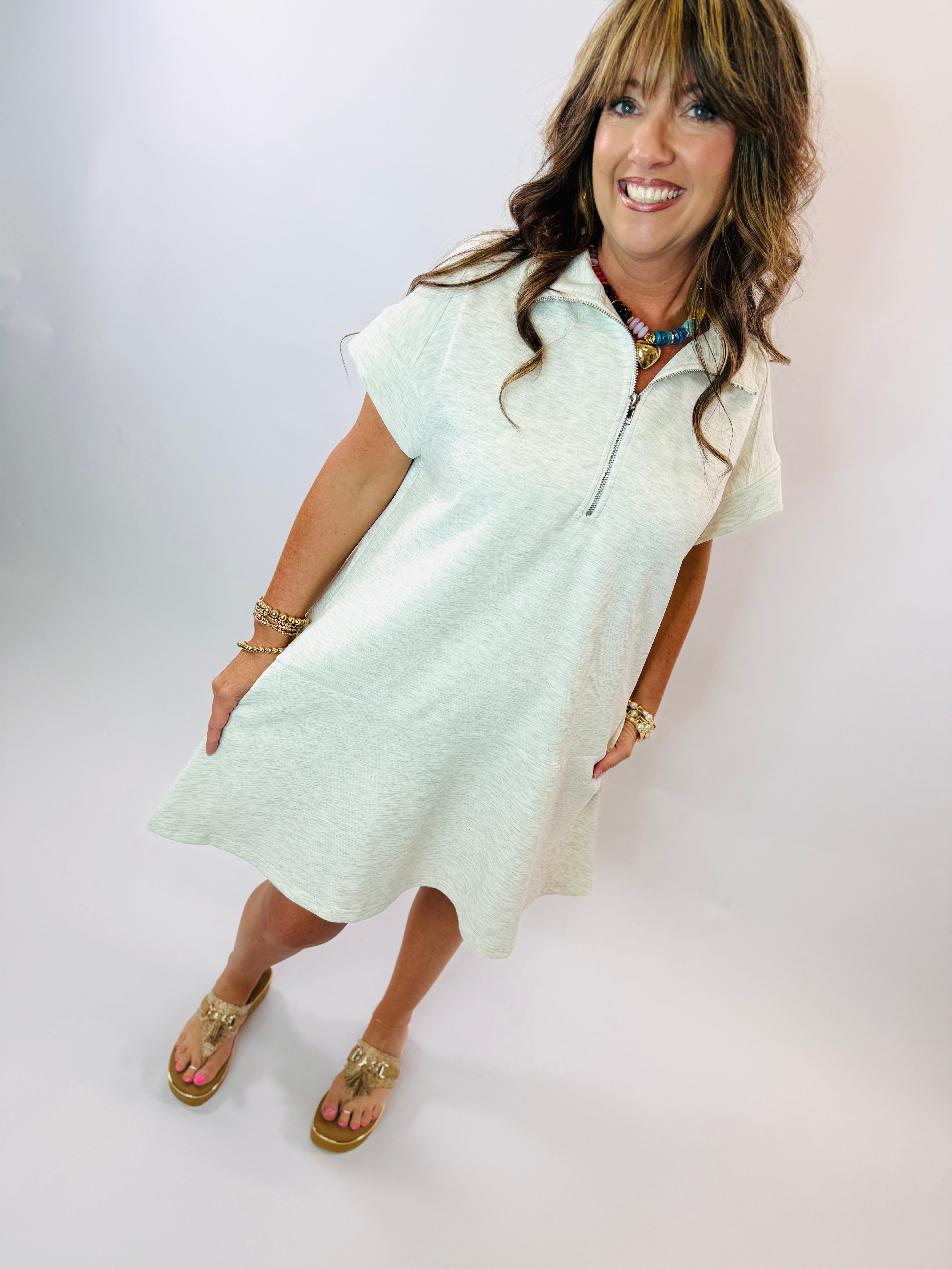 Woman wearing light green heather casual dress with zipper neckline, gold sandals and jewelry accessories.