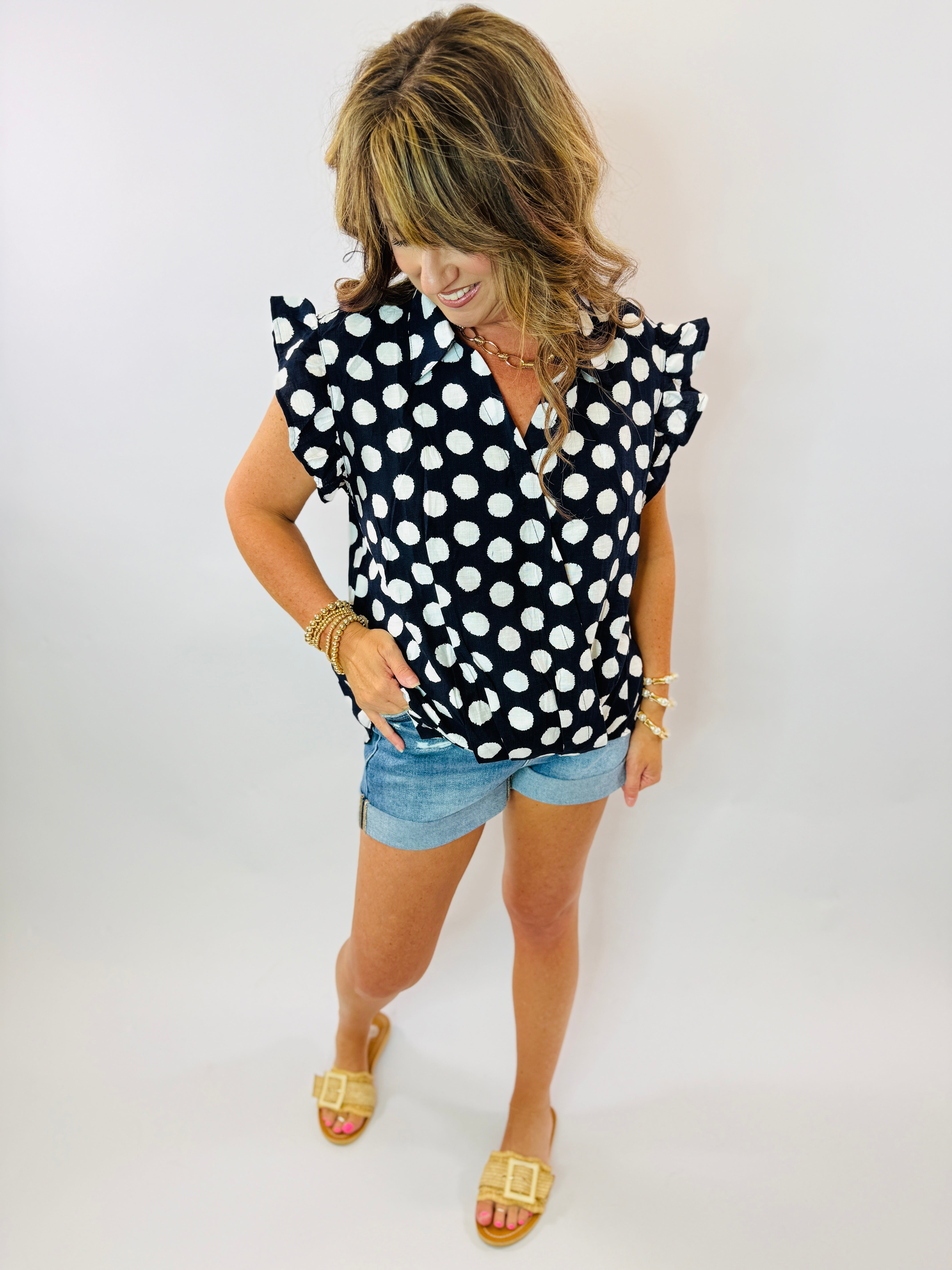 Woman wearing black and white polka dot ruffled sleeve top with denim shorts and gold sandals