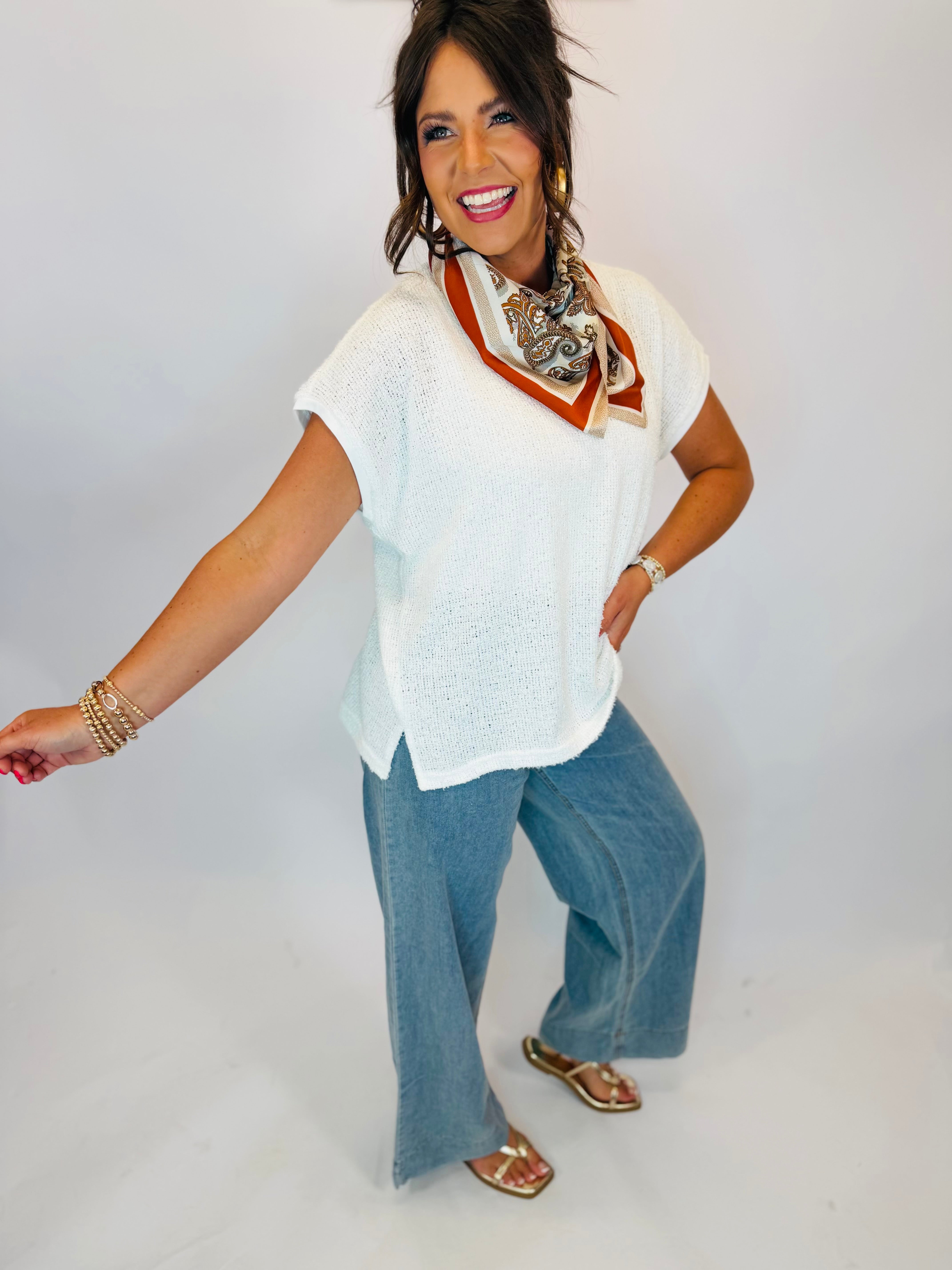 Woman wearing white knit sleeveless V-neck top styled with wide-leg jeans and paisley neck scarf.